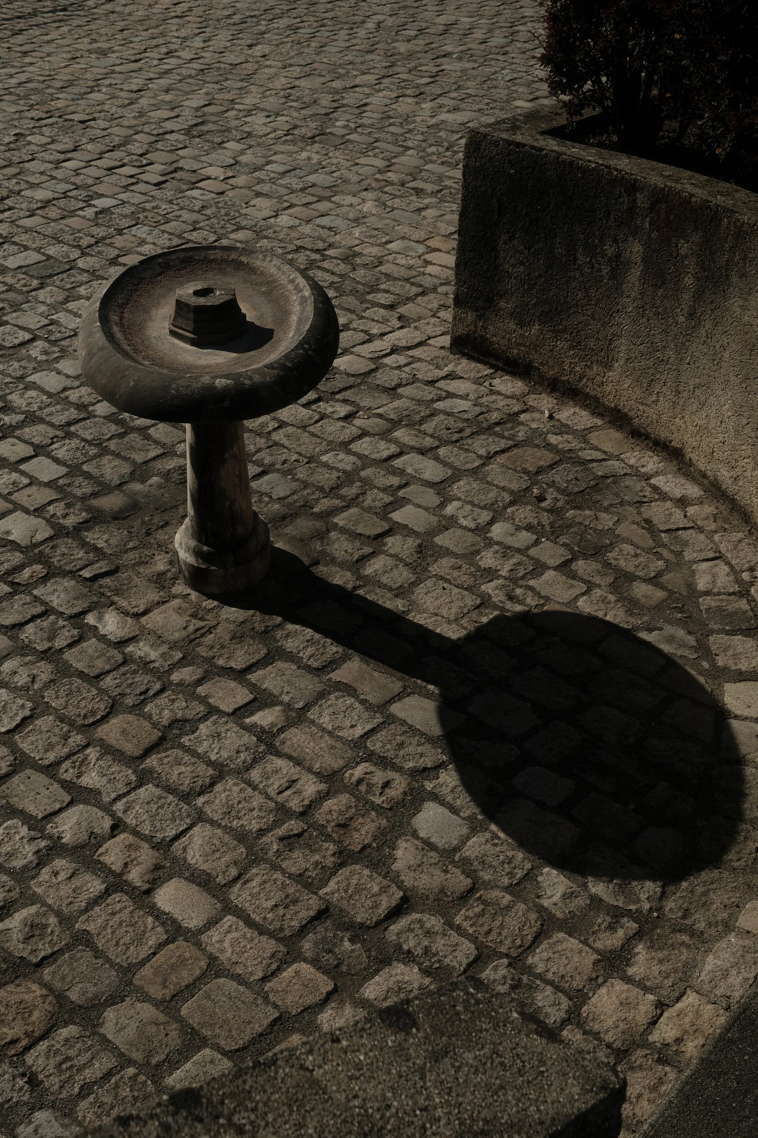 Top-down view of urban geometry. Shadows and textures on paved ground with a solitary rock. Conceptual street photography.