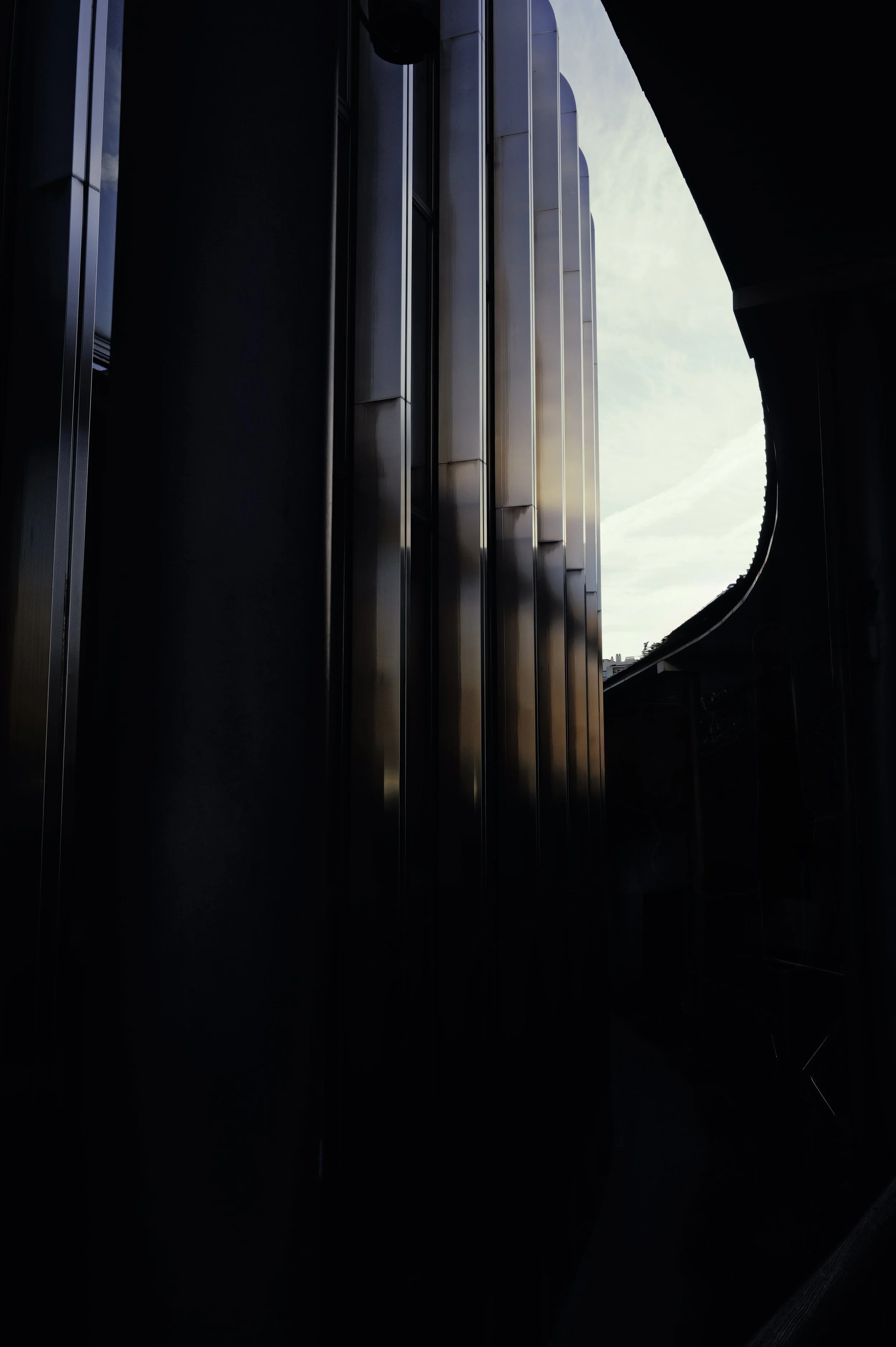 High-contrast architectural photography: dark metallic vertical columns and deep shadows against a bright background.