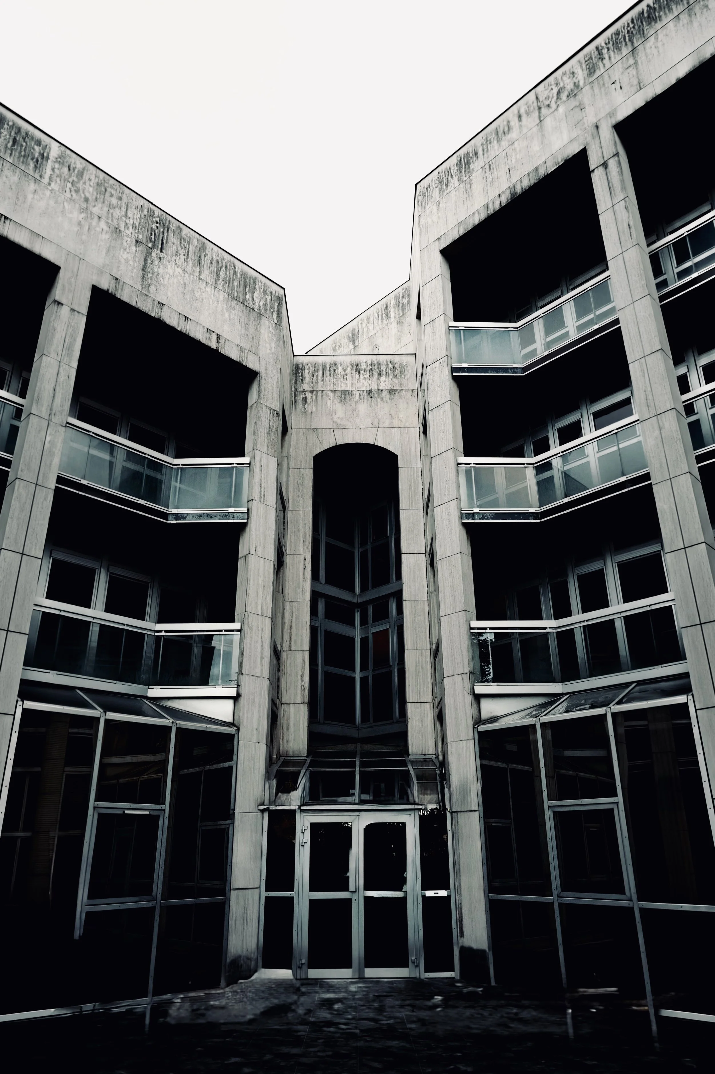 Angular concrete building surrounding a recessed central entrance, with stacked windows and balconies.