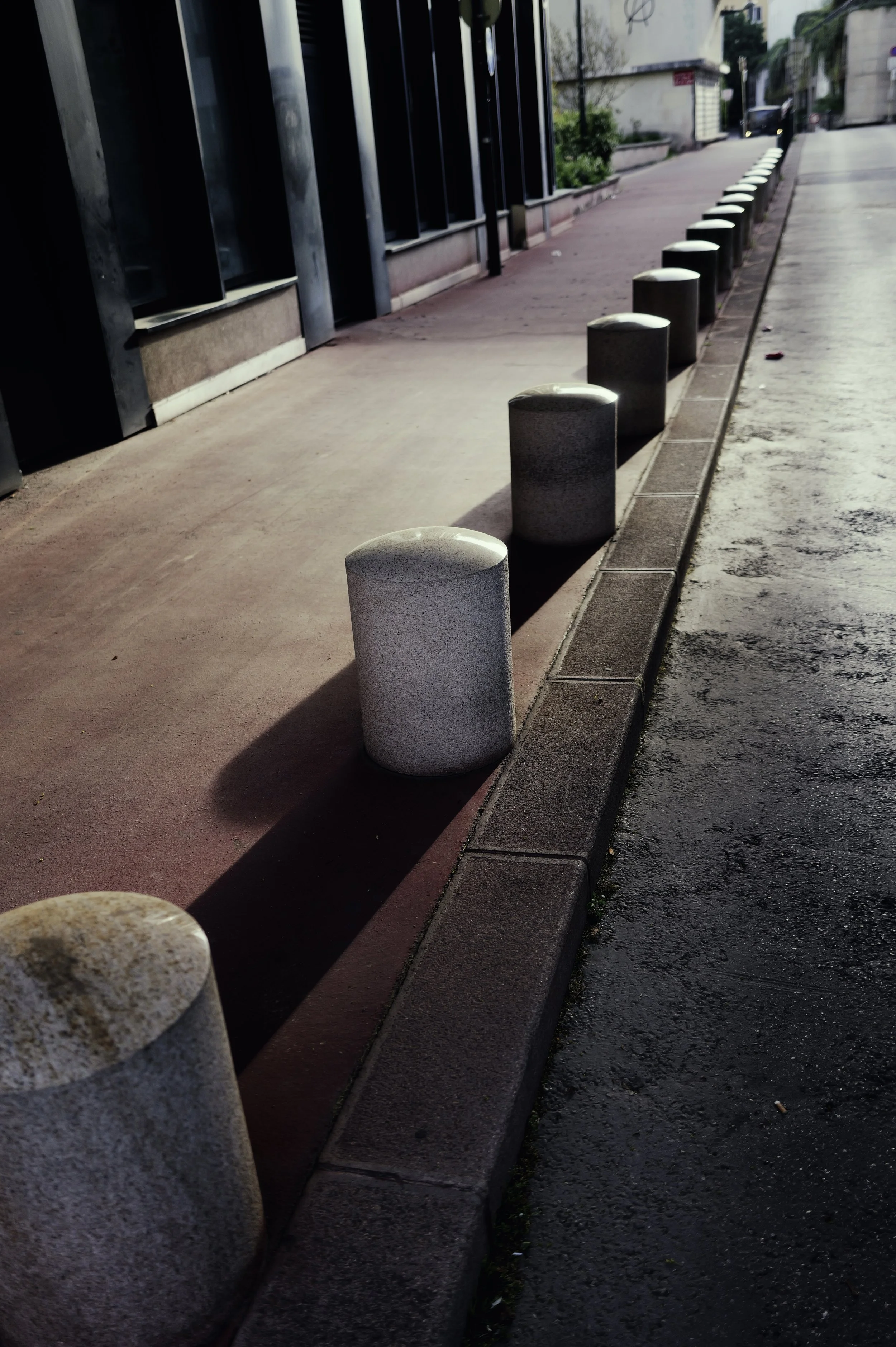  Perspective and leading lines in an urban street at sunset. Concrete bollards on a paved sidewalk. Urban Chrome aesthetic.