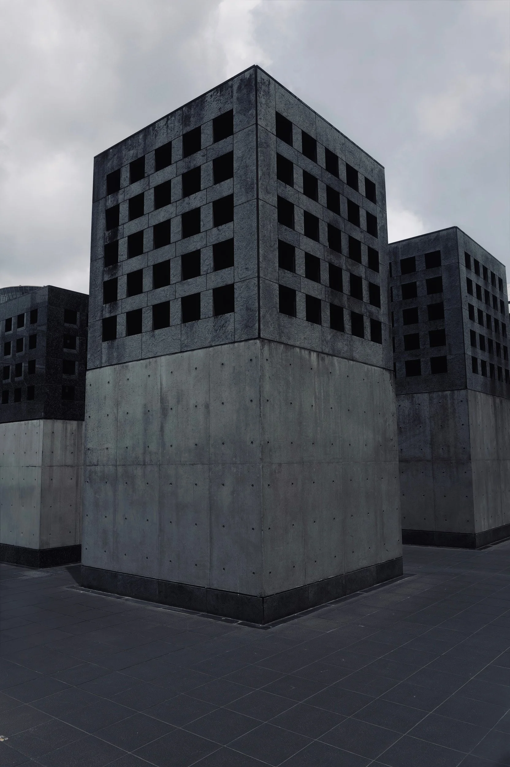 Three massive concrete structures with grids of dark square openings beneath an overcast sky.