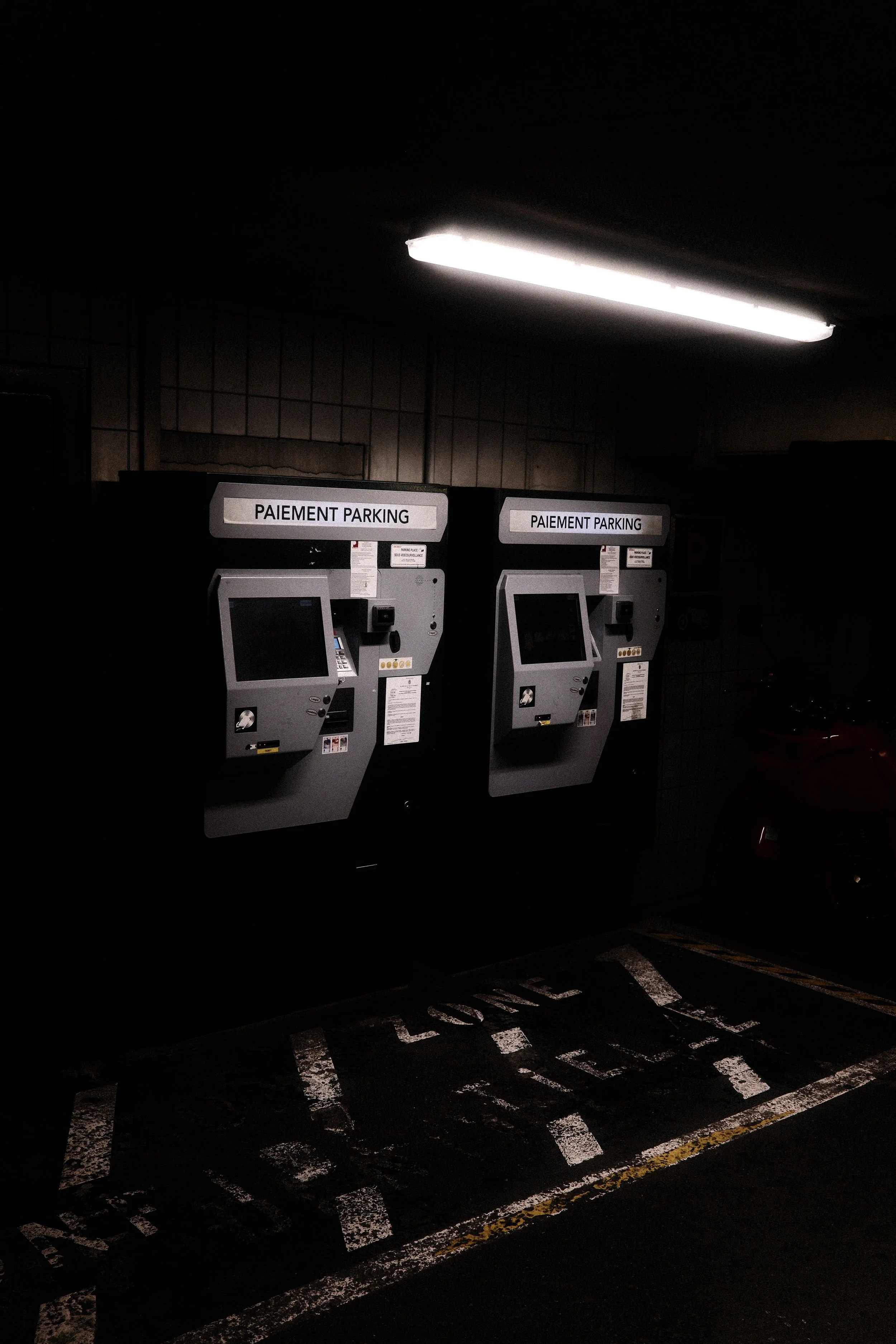Moody cinematic street photography of a parking payment station at night. Low light, shadows, and urban solitude.