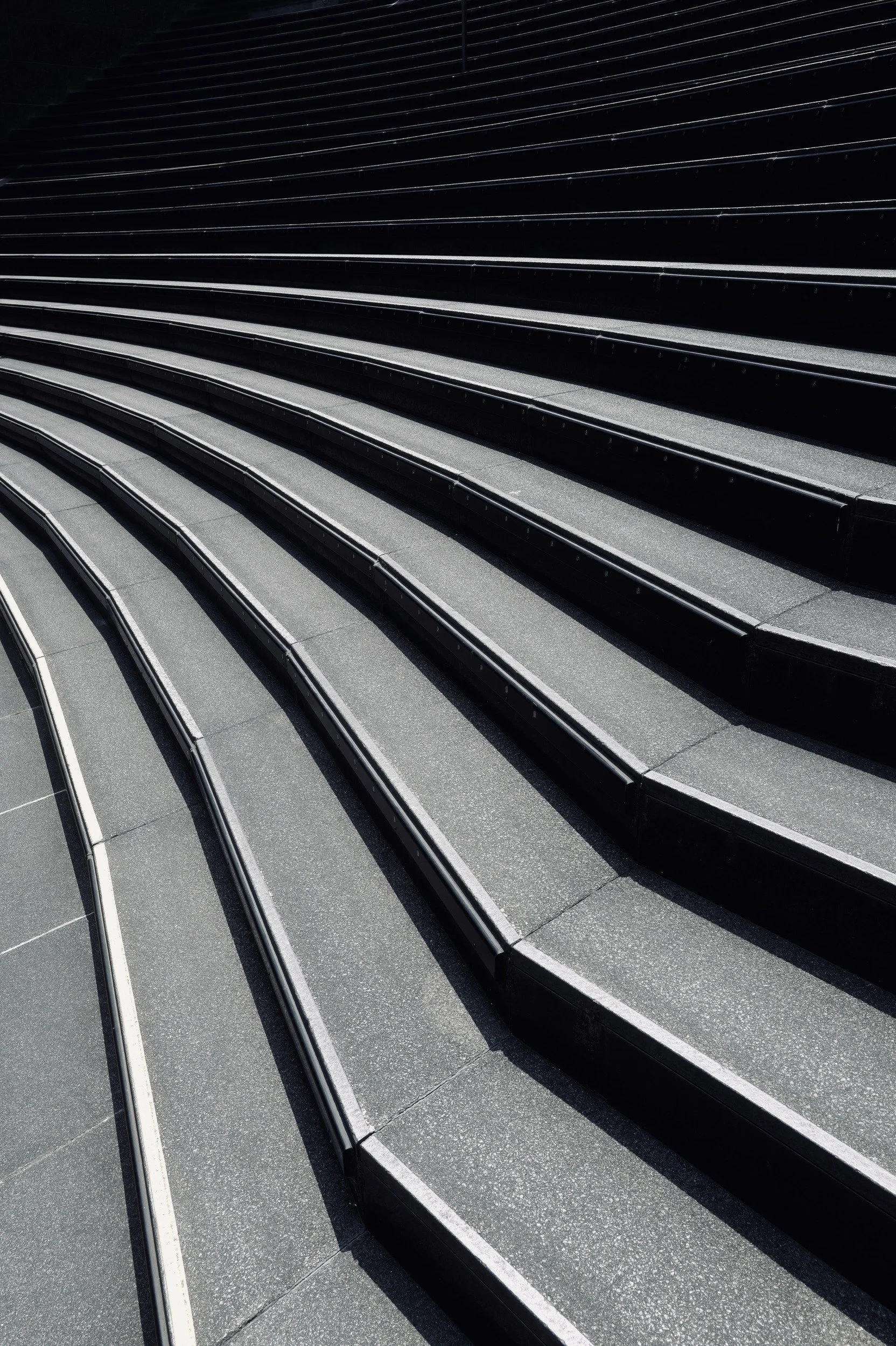 Broad curved steps traced by parallel metal strips and sharp black shadows.