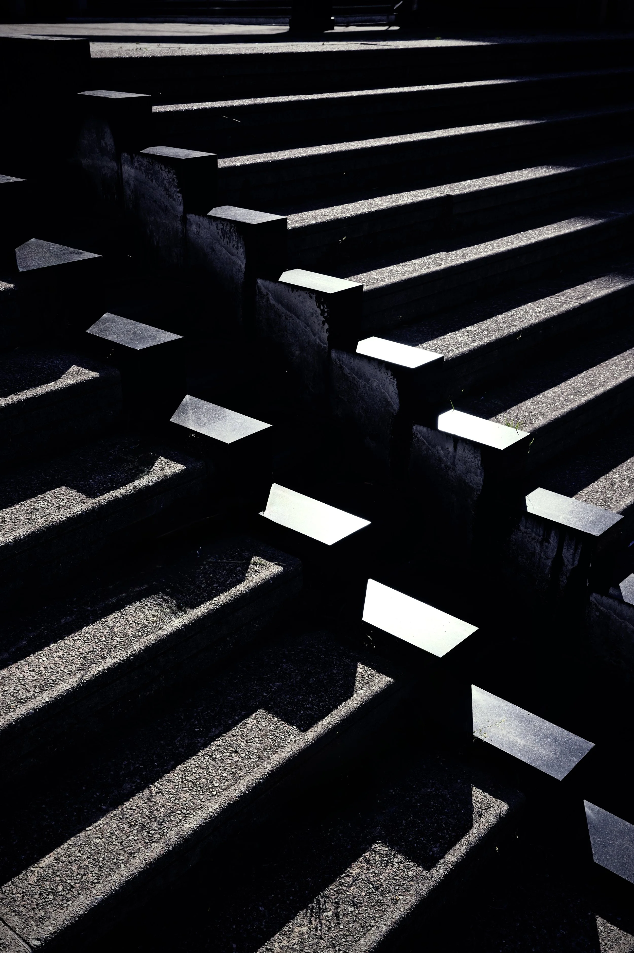 High-contrast architectural photography of stone steps with sharp sunlight patterns. Graphic shadows and urban geometry.