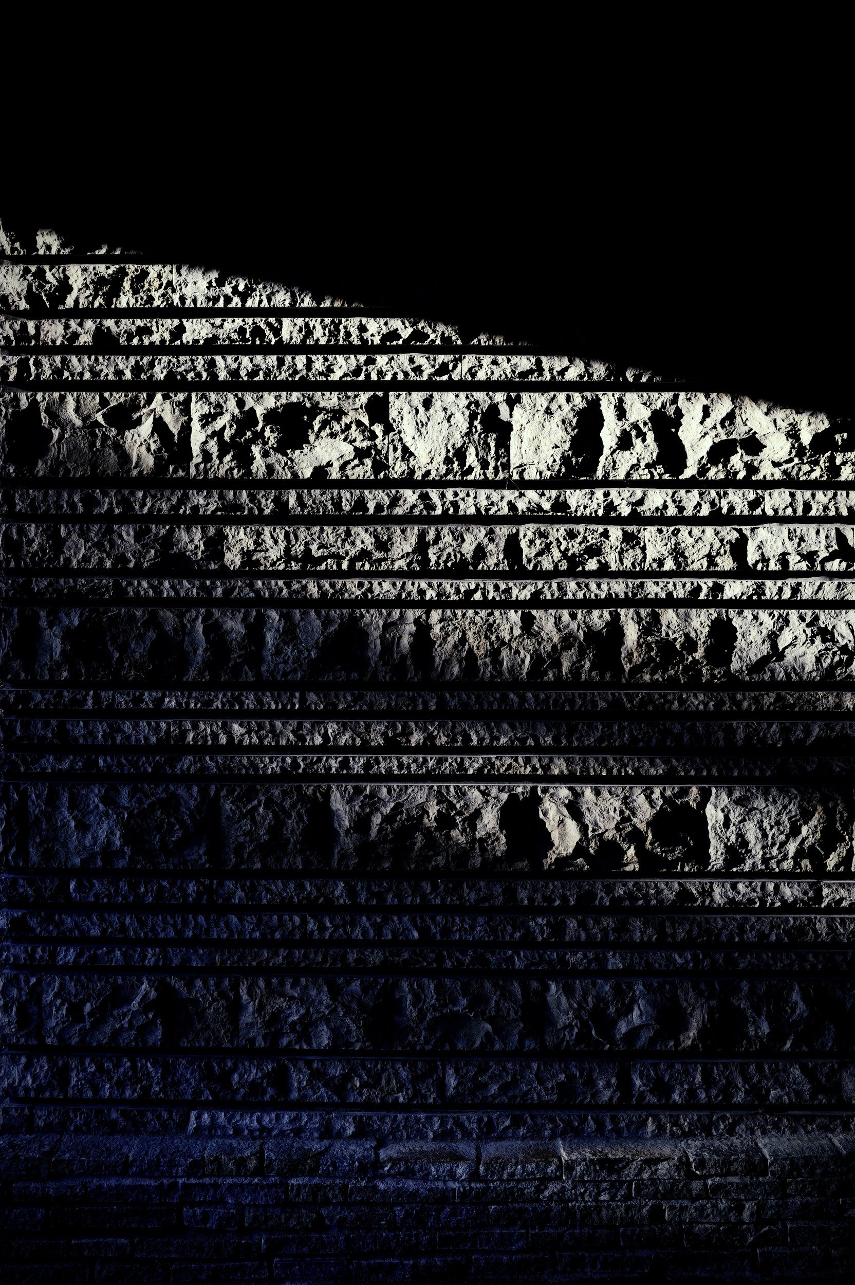 Rough stone courses and horizontal bands crossed by a wedge of hard light.