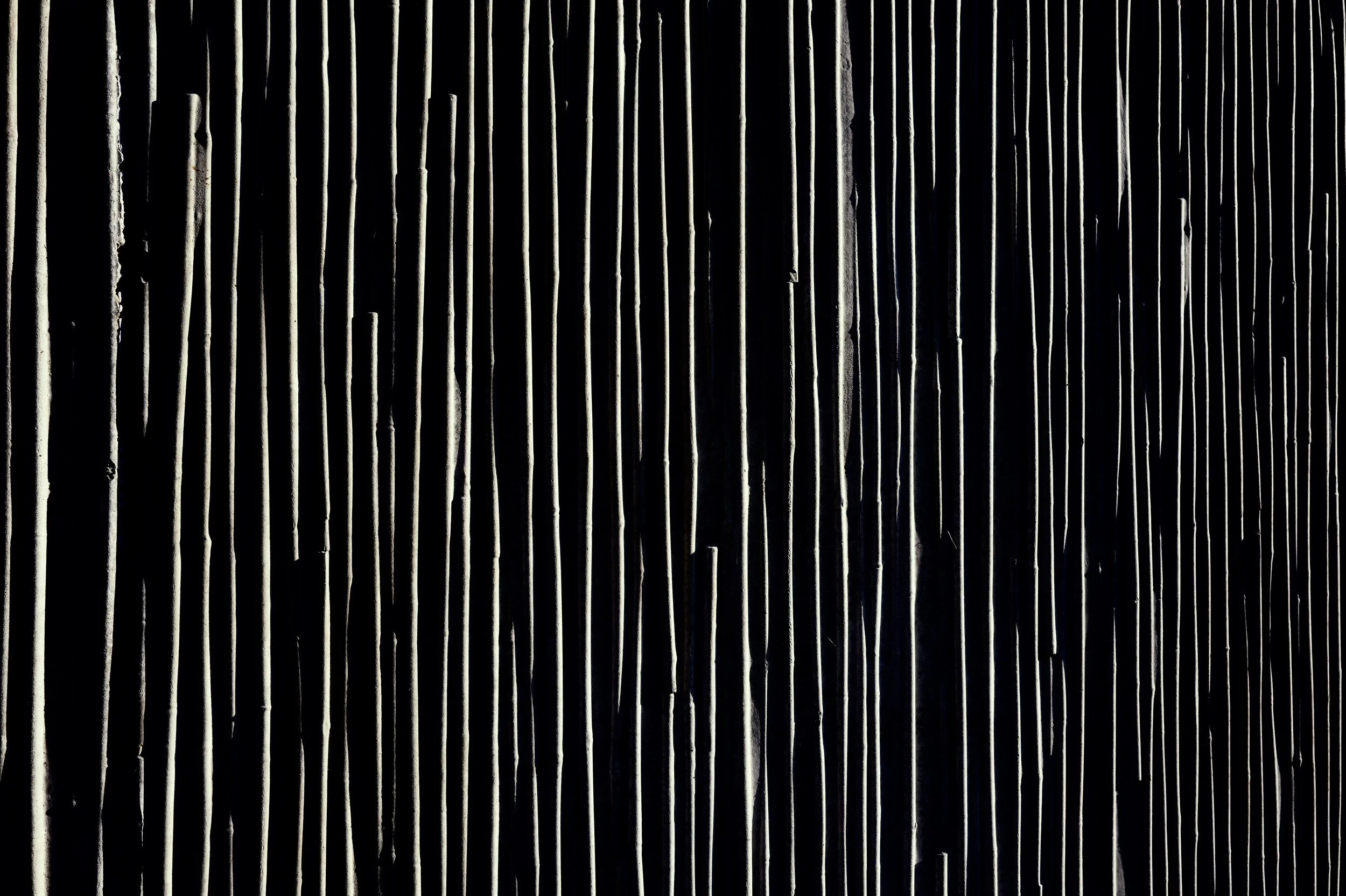Thin irregular vertical ridges picked out by light against a black surface.