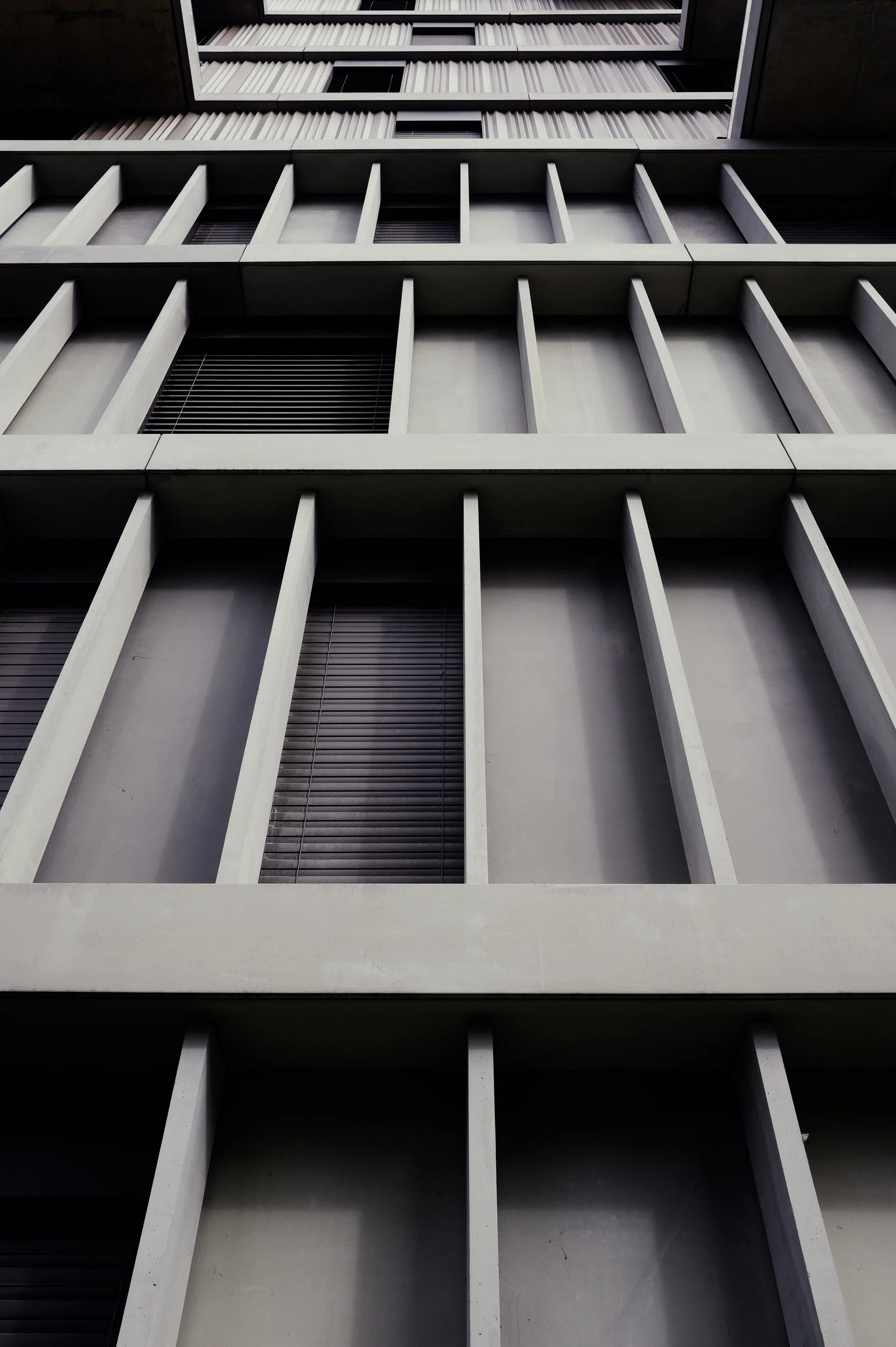 Pale vertical fins and recessed dark windows rising in a tightly framed facade.