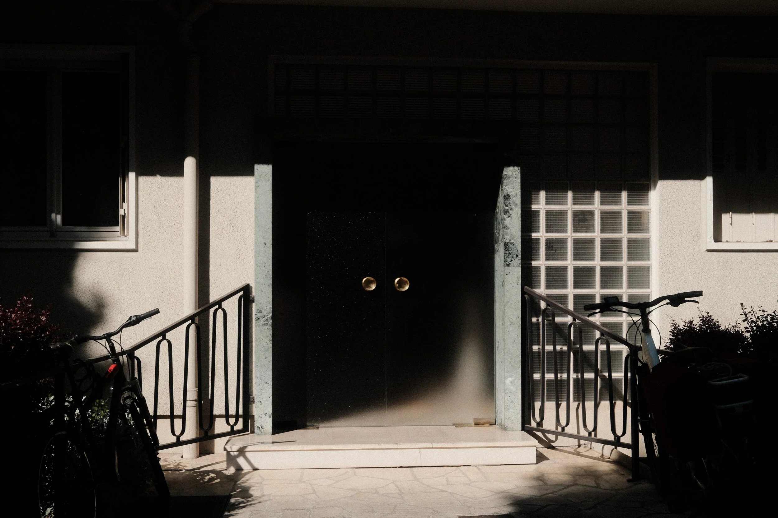 Cinematic night photography of a house entrance with parked bicycles. Contrast between light and deep shadows.