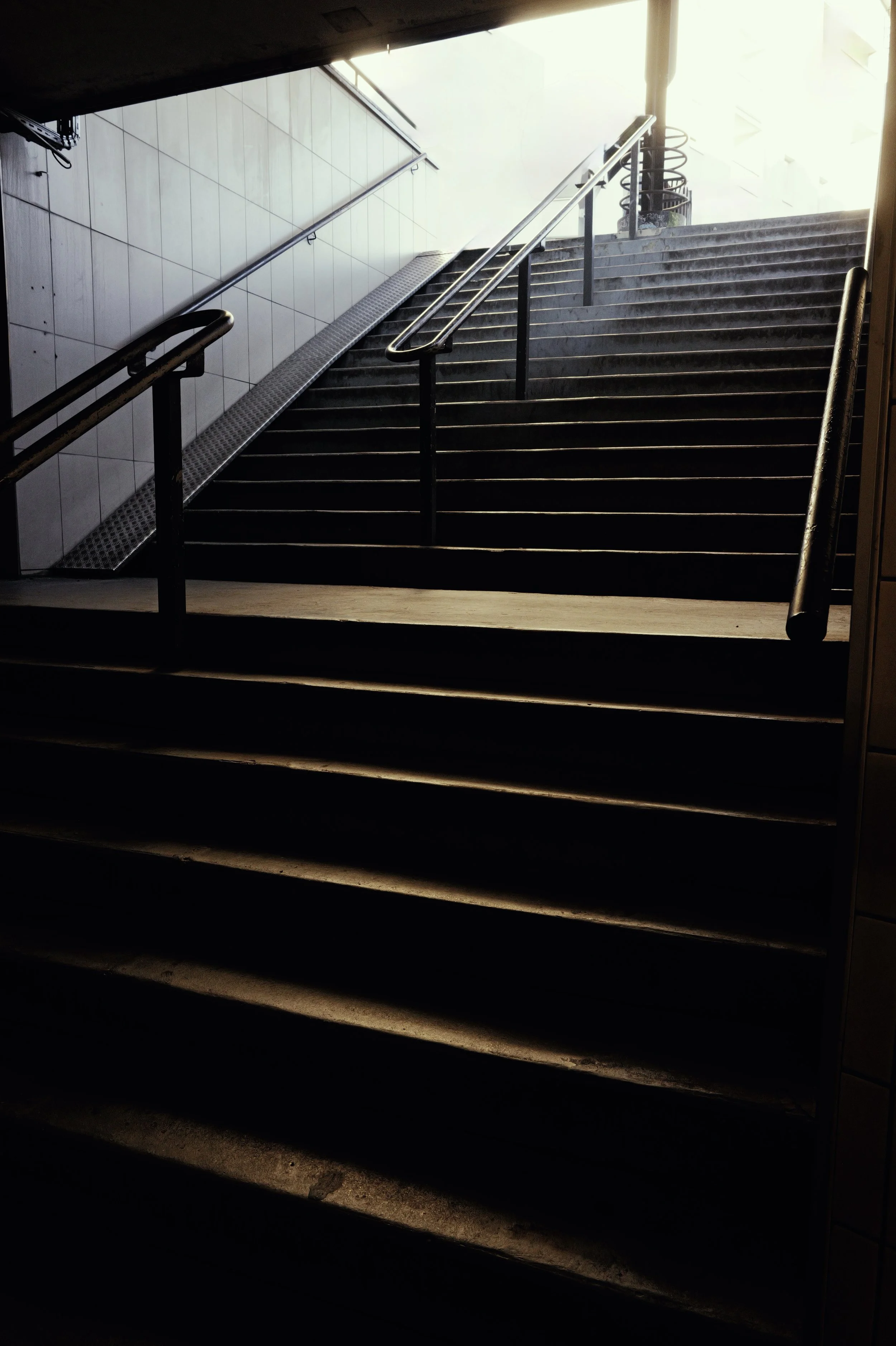 Moody architectural photography of an interior staircase. Dramatic natural lighting and vertical geometric lines.