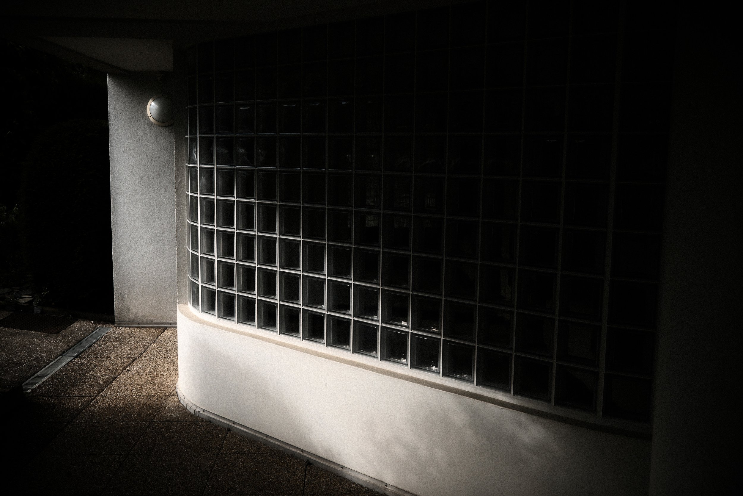 Architectural photography of a glass block window on a concrete façade. Minimalist light and texture study.