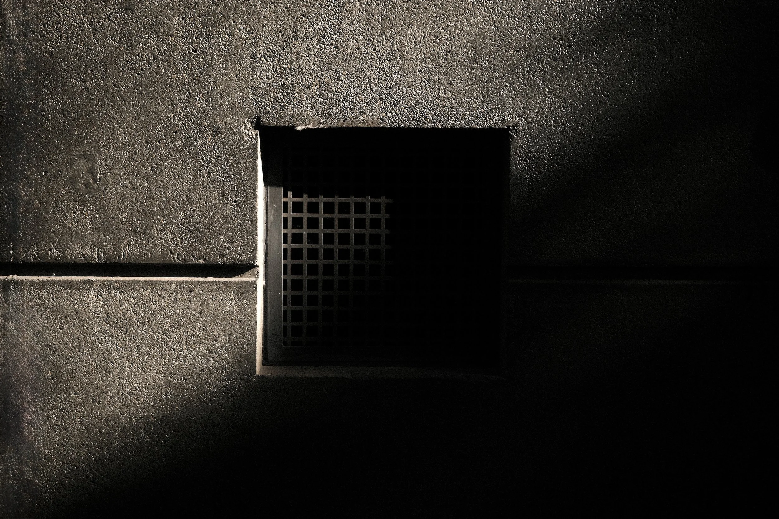 Macro urban photography of a metal manhole cover. High-contrast texture of grainy concrete and industrial patterns.