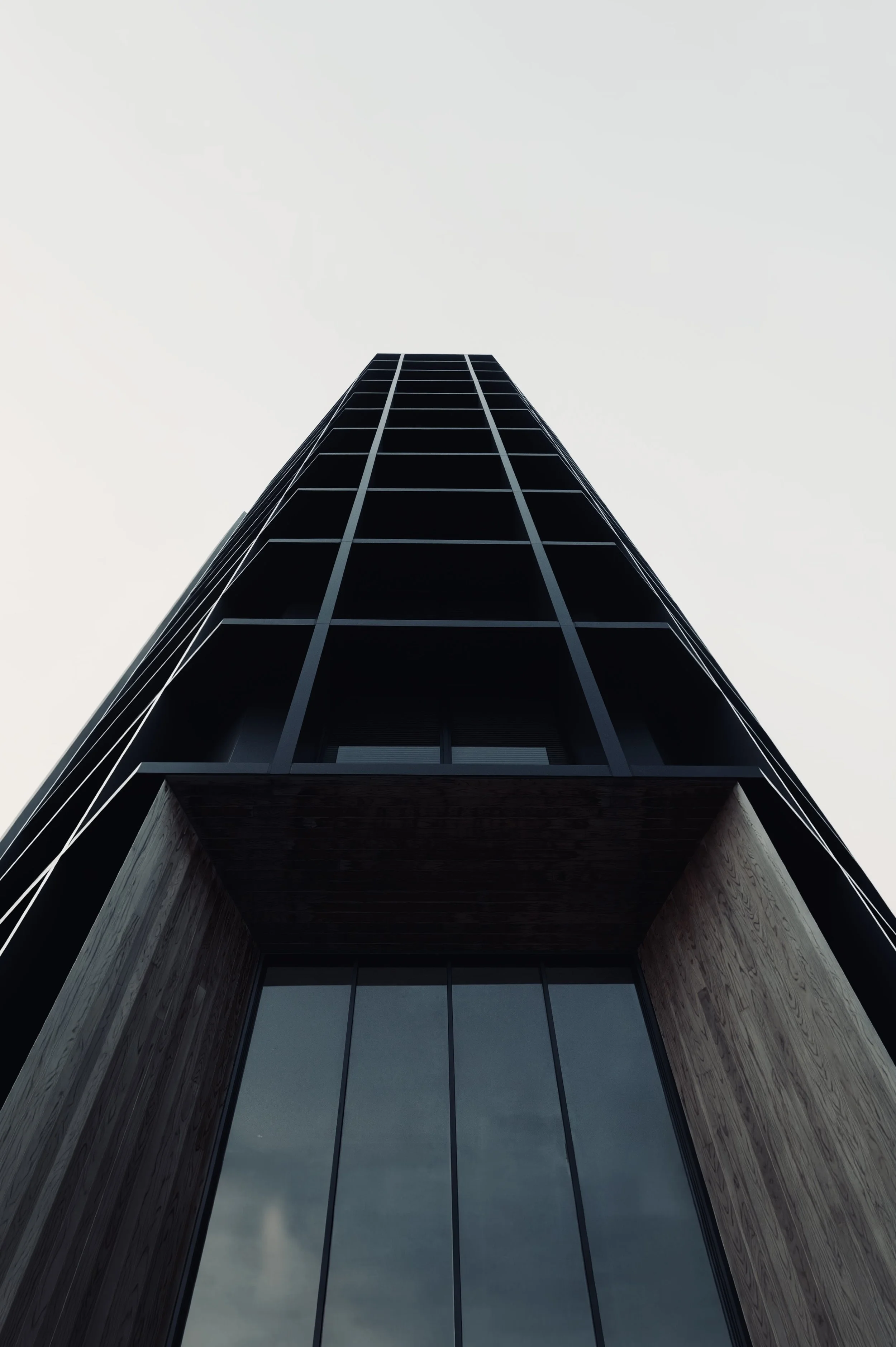 A narrow dark tower seen symmetrically from below, with a rigid window grid rising above a recessed glass entrance.