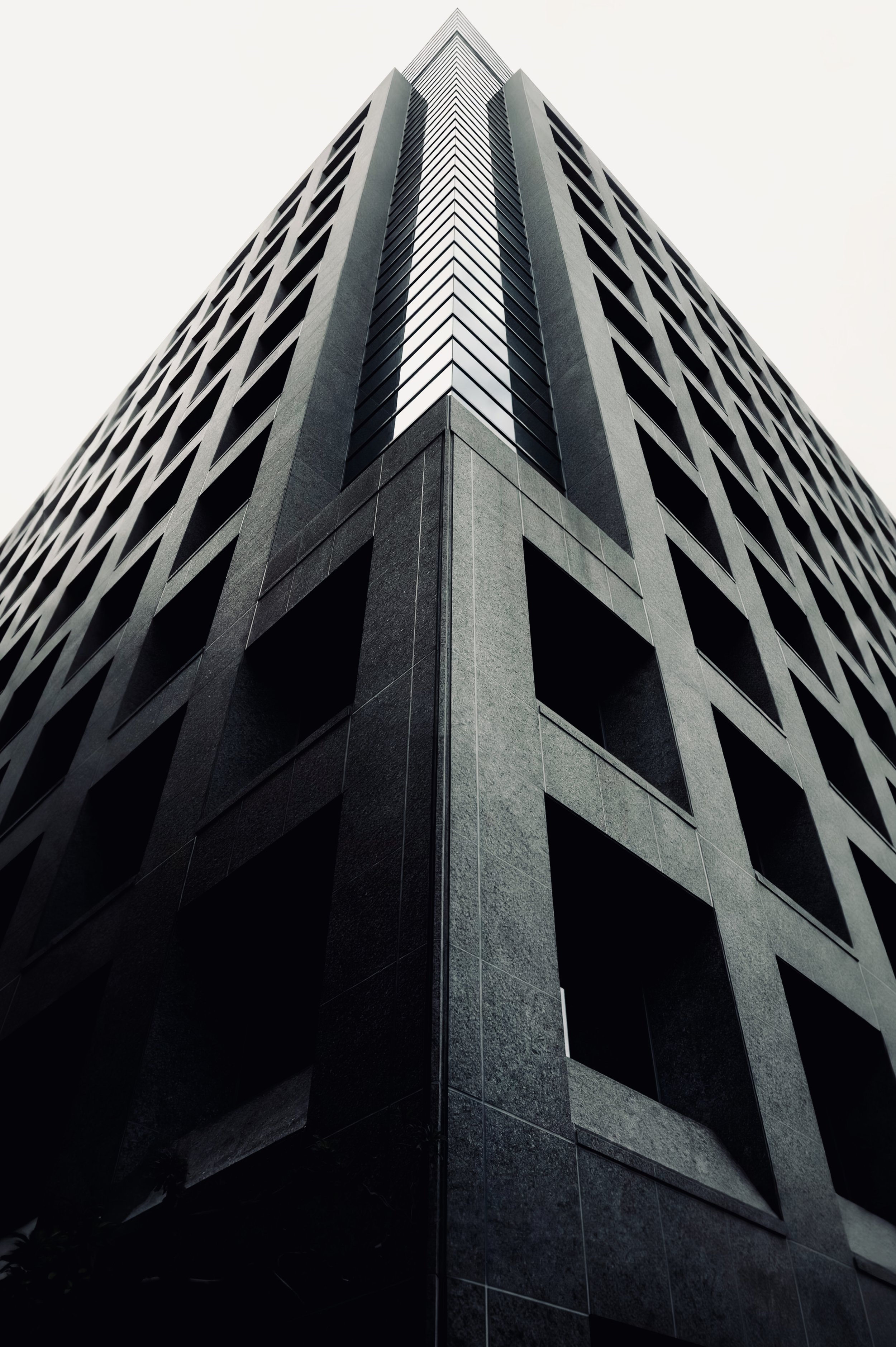 Low-angle view of the corner of a tall geometric building with repeating rectangular facade openings.