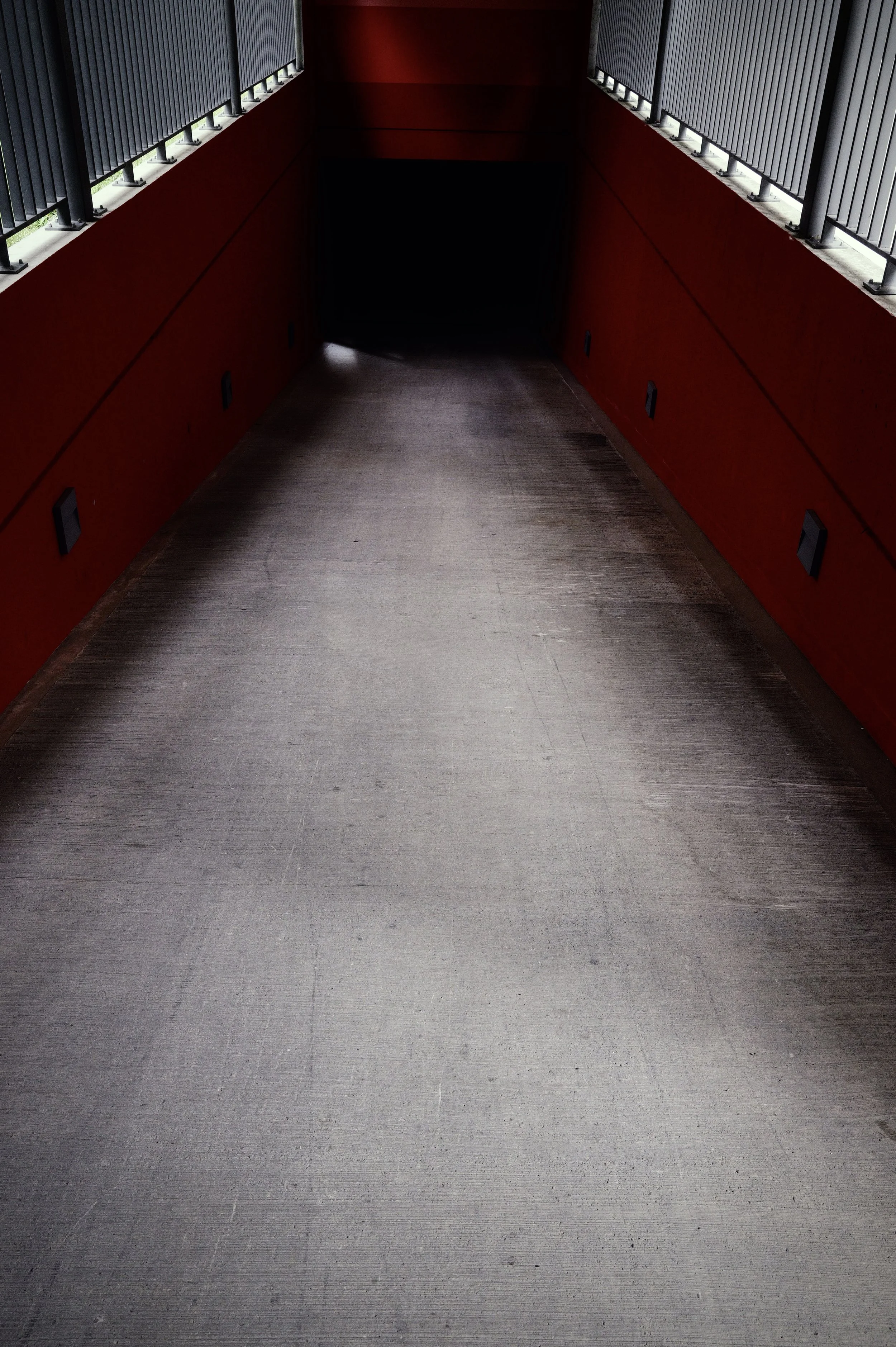 Cinematic street photography of a minimalist urban underpass, dark walls framing a leading perspective with moody light