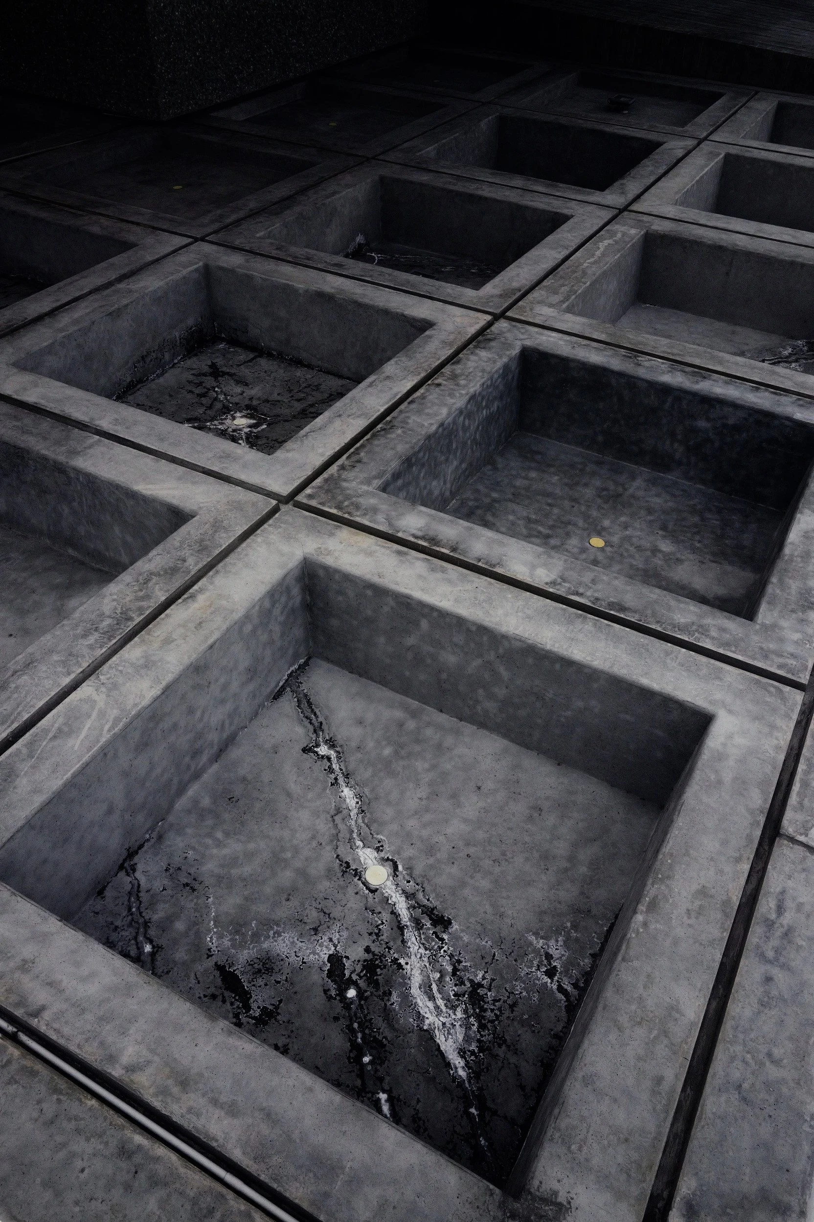 Rectangular concrete basins seen obliquely from above, with cracks and deep recesses.