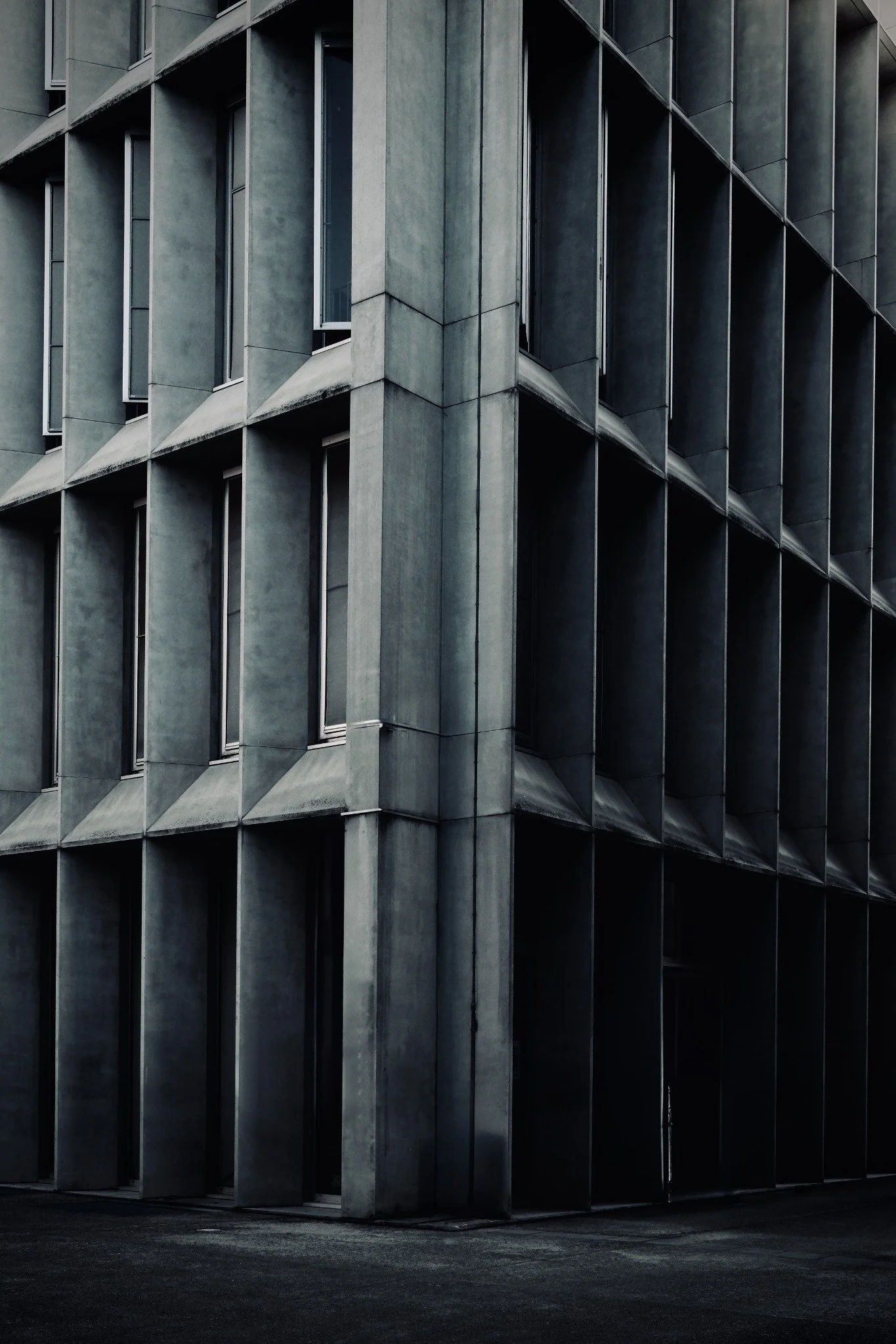 Corner of a grey concrete facade with repeated deep window recesses and dark shadows.