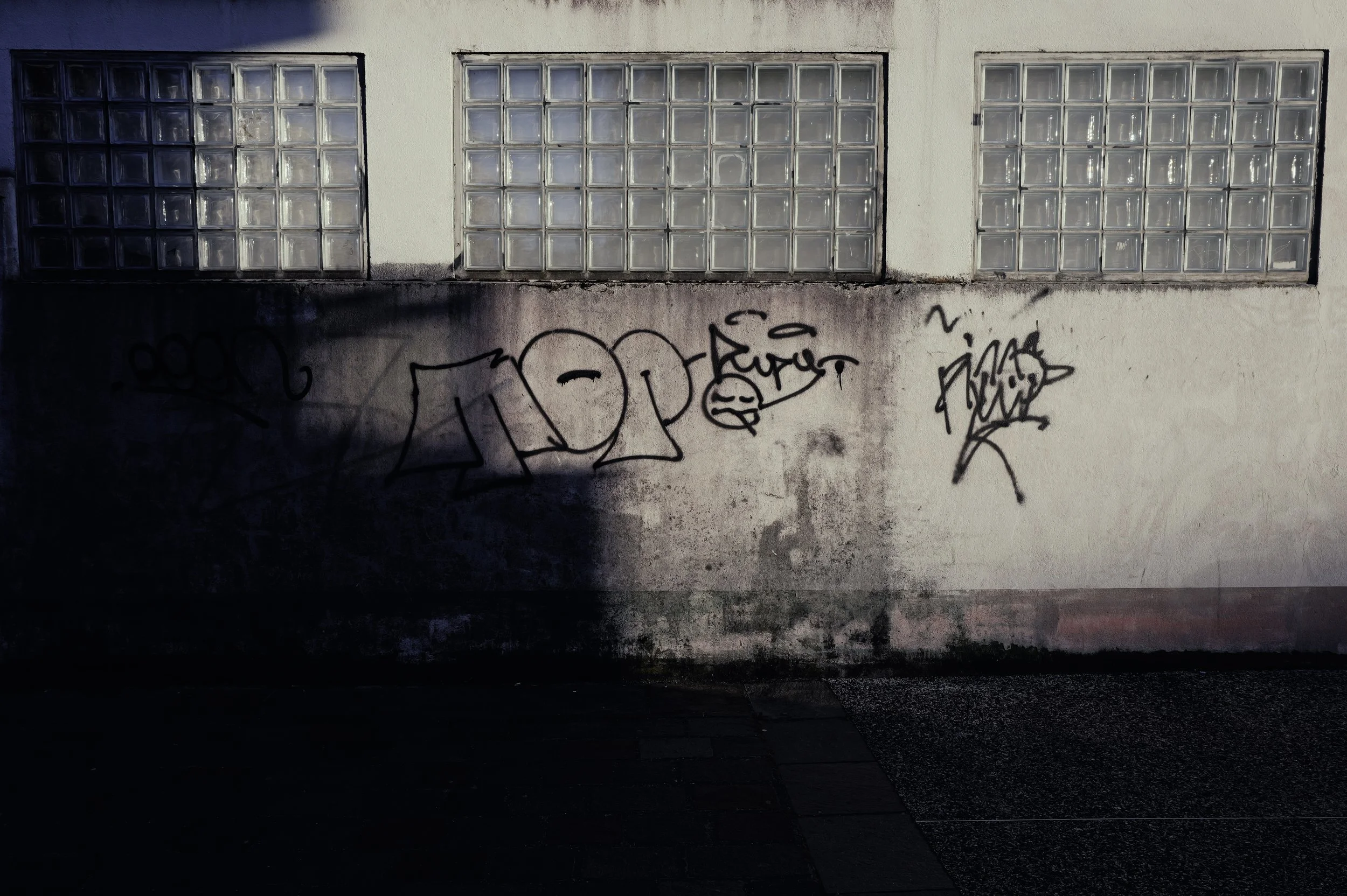 Gritty urban landscape showing broken windows and graffiti on a white wall. Texture, grain, and urban decay.