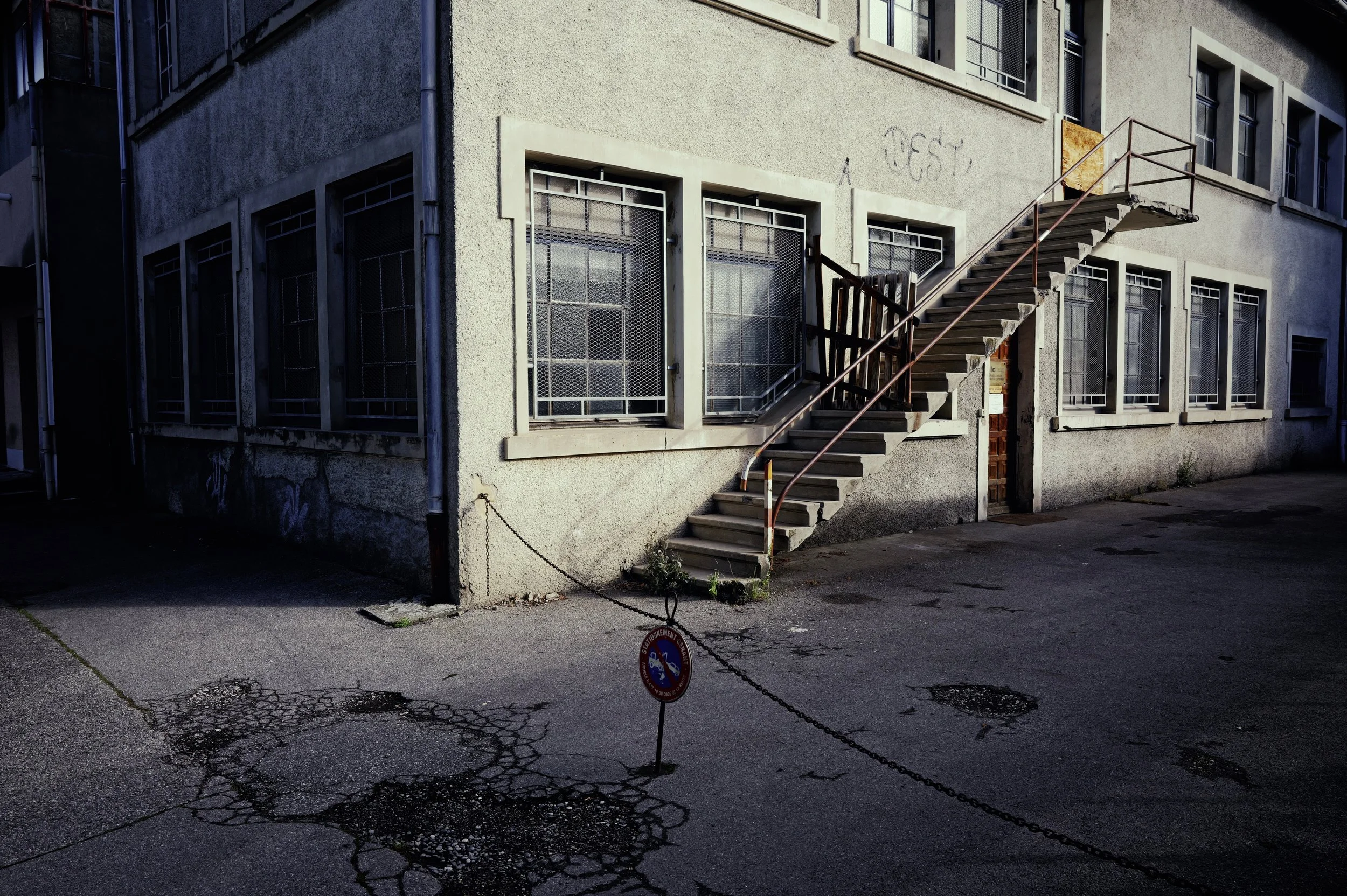 Minimalist urban photography of a concrete building façade with an exterior staircase and geometric shadows. Urban Chrome style.