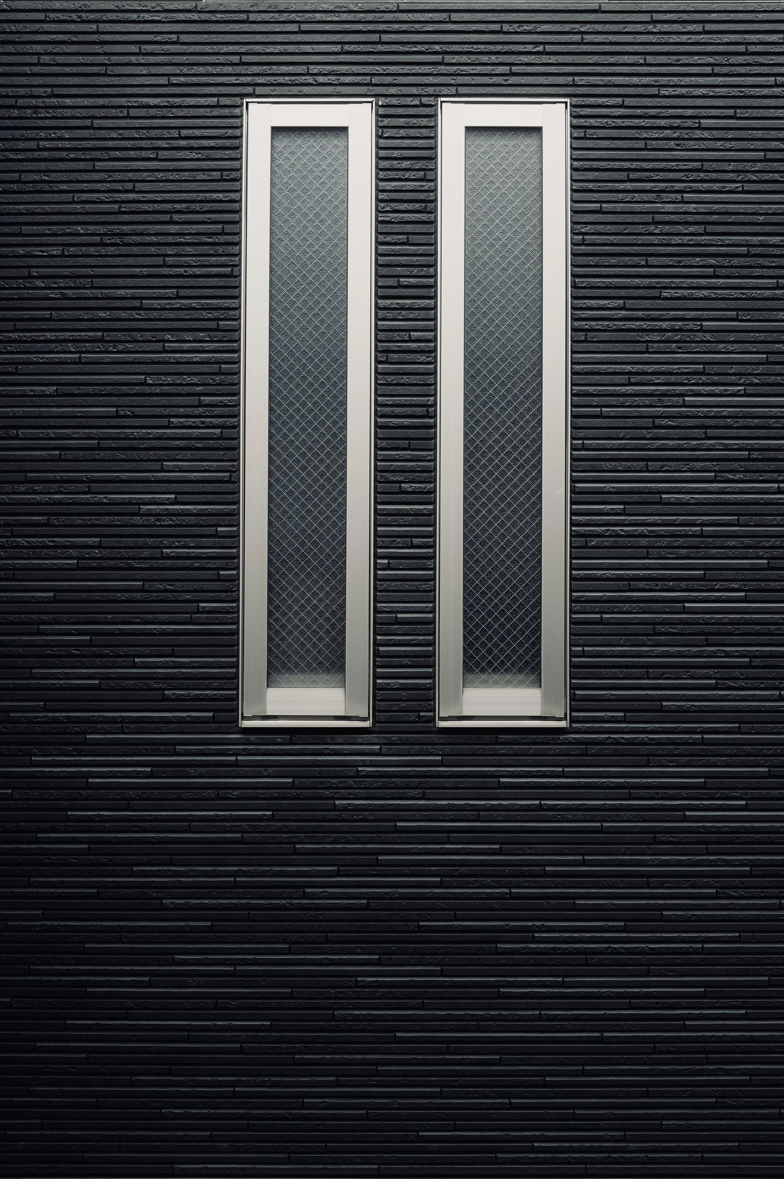 Symmetrical narrow windows on a dark textured cladding wall - Minimalist architectural detail - Urban fine art photography