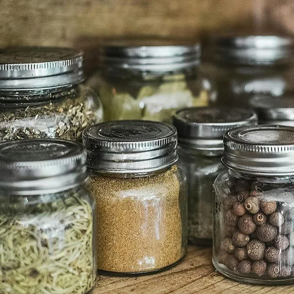 Organise & Harmonise. Several small glass jars with silver lids filled with spices and herbs on a wooden surface.