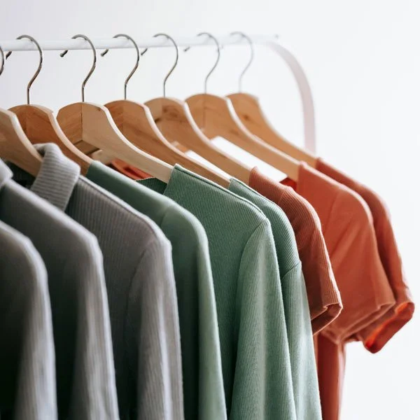 Organise & Harmonise. A row of colourful sweaters hanging on wooden hangers on a white clothing rack.