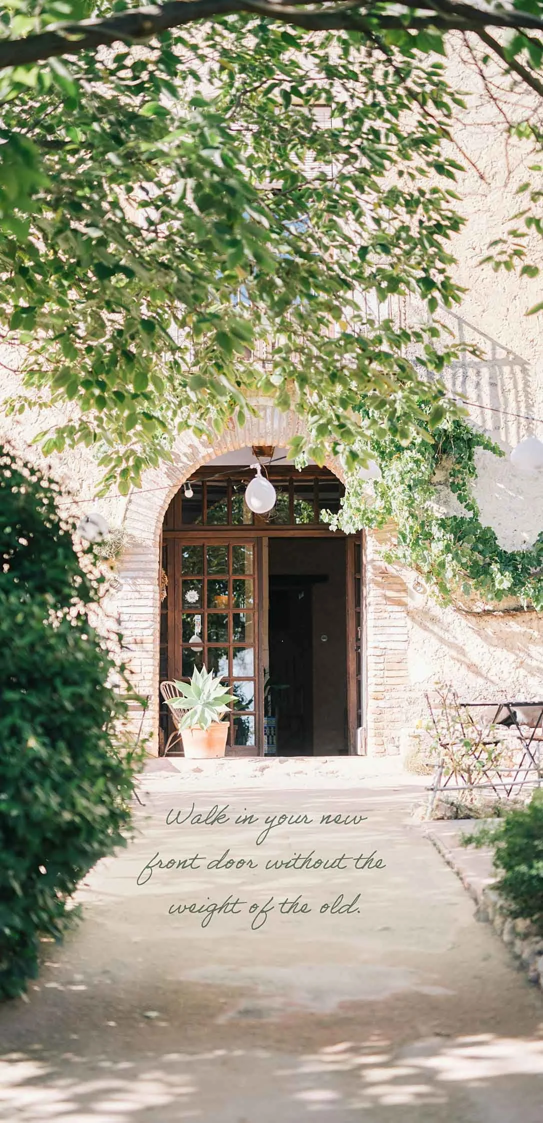 A charming brick and white stucco house entrance with a wooden door, surrounded by lush green foliage and potted plants. Text overlay reads, "Walk in your new front door without the weight of the old."