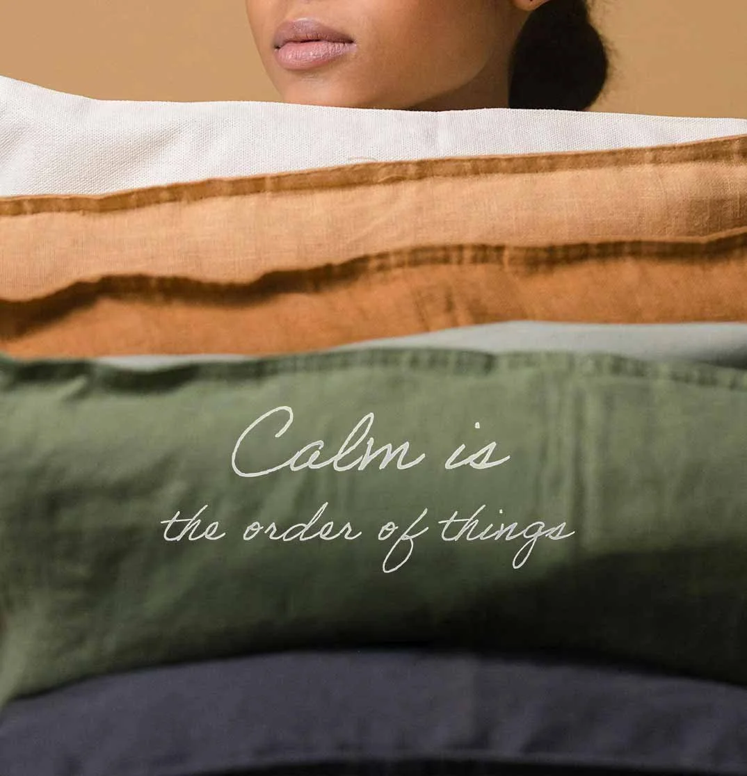 Close-up of a woman's face behind a stack of multicolored fabric or clothing with the text "Calm is the order of things" written on the green fabric.