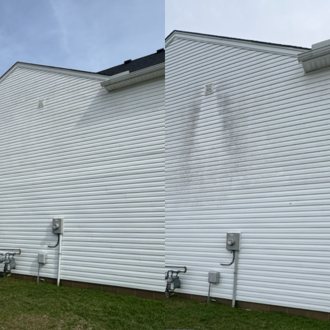 Side view of a white house wall with horizontal vinyl siding, showing black soot or dirt stains around a vent and utility meters.