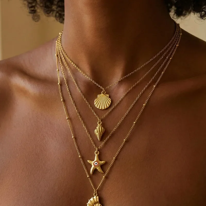 Une personne porte plusieurs colliers dorés avec des pendentifs de coquillage, étoile de mer, et autres motifs marins.