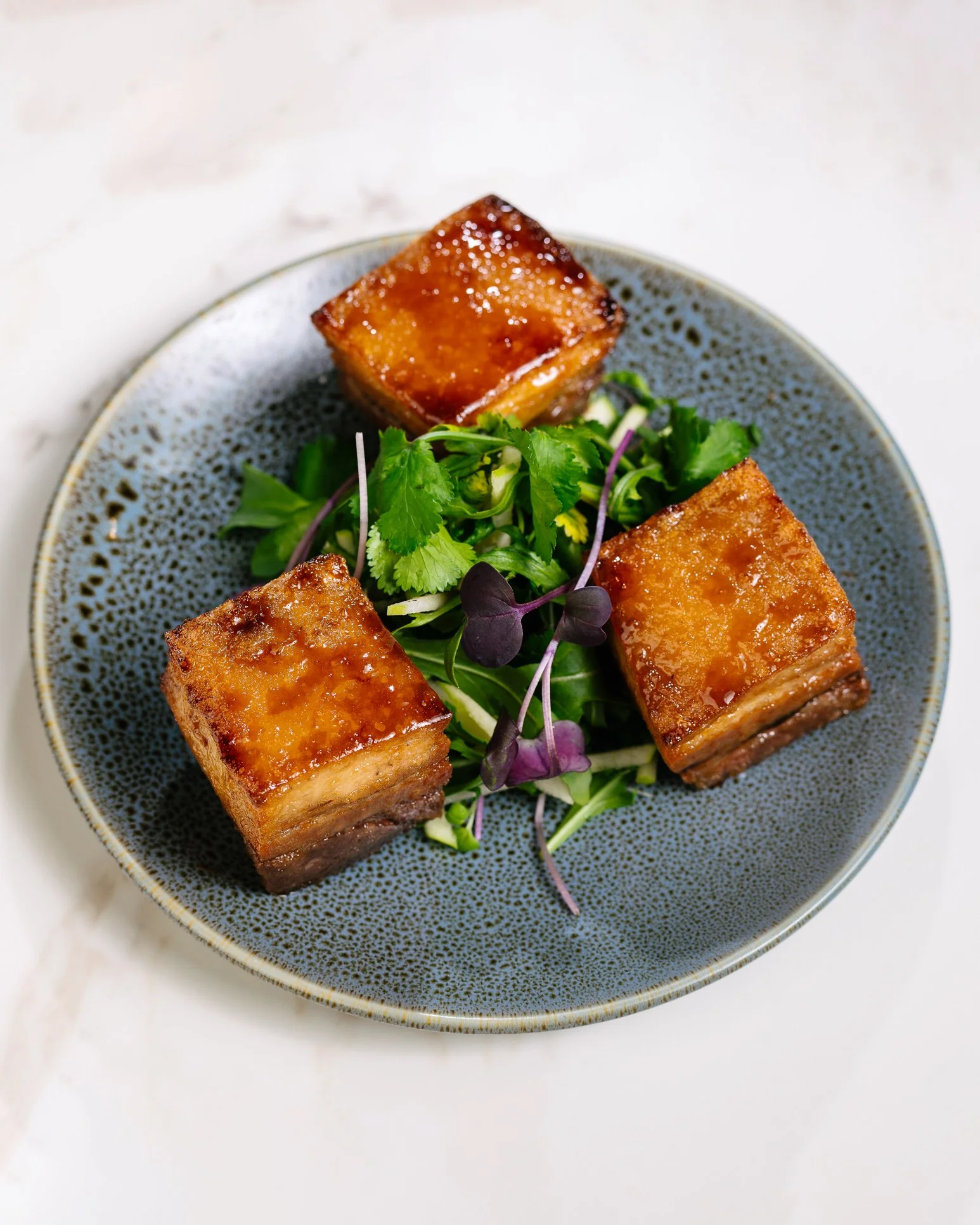 A plate with three pieces of glazed tofu and a small side salad of mixed greens.