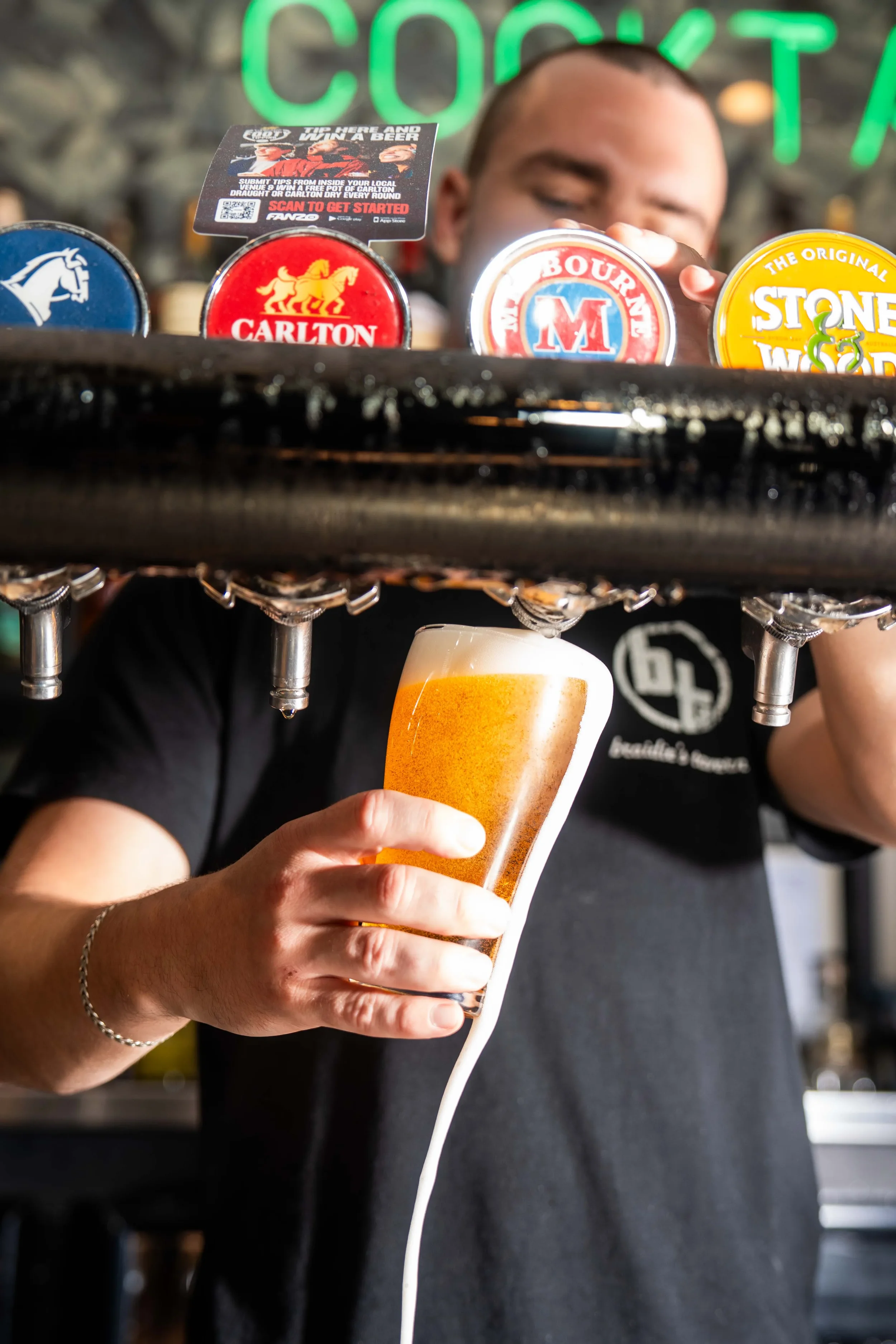 Man pouring beer from a tap at a bar, with a glass of beer in his hand.