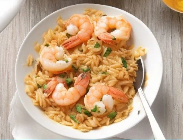 A bowl of shrimp pasta garnished with chopped green herbs, sitting on a wooden table with a fork and a napkin.