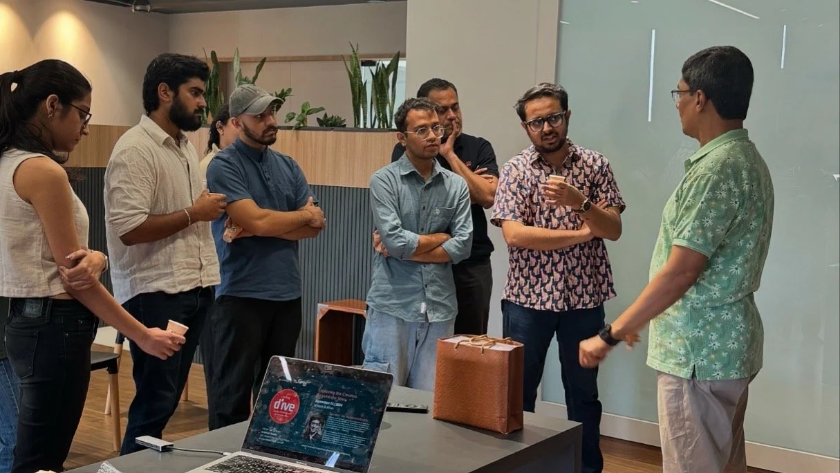 Group of seven people standing in a semi-circle, engaged in a discussion in a modern office space.