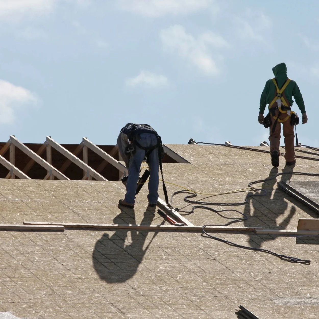 Two construction workers installing roofing on a building under a blue sky.