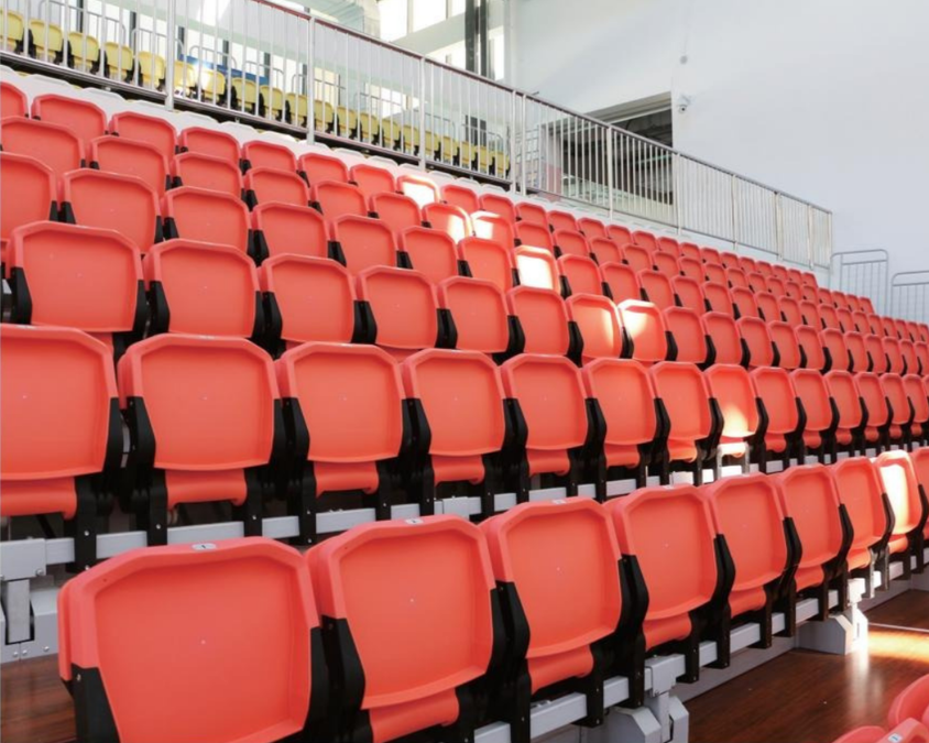 Empty orange and yellow stadium seats in an indoor arena.