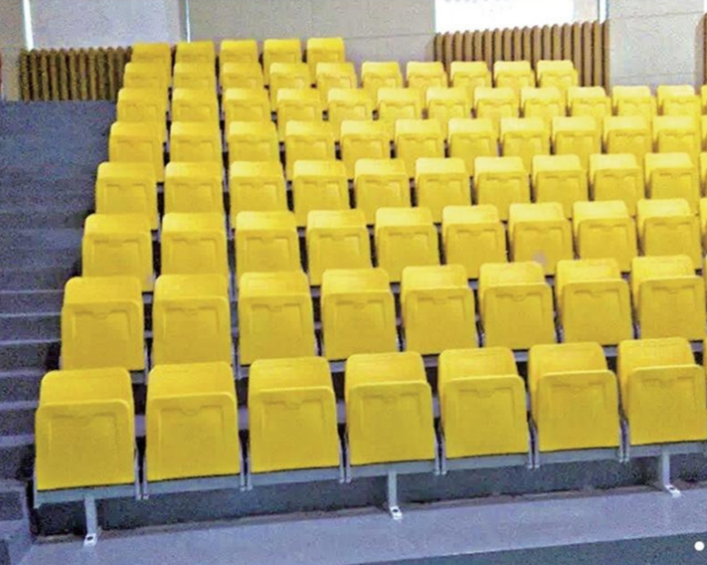 Empty yellow stadium seats arranged in rows and stairs leading up on the left side.