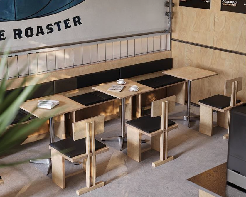Wooden tables and chairs in a cafe or restaurant, with some cups and a book or menu on the table. There is a banner on the wall behind the seating area.