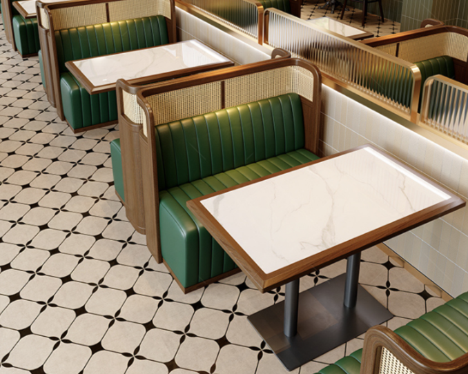 Empty booth seating with green upholstered benches and marble tables in a restaurant with patterned tile flooring.