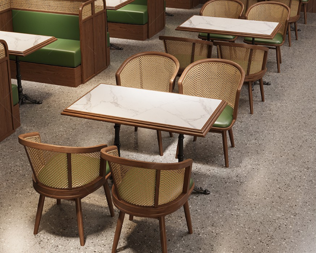 Empty restaurant with green booth seating, marble-top tables, and wooden chairs with cane backs, on a speckled gray floor.
