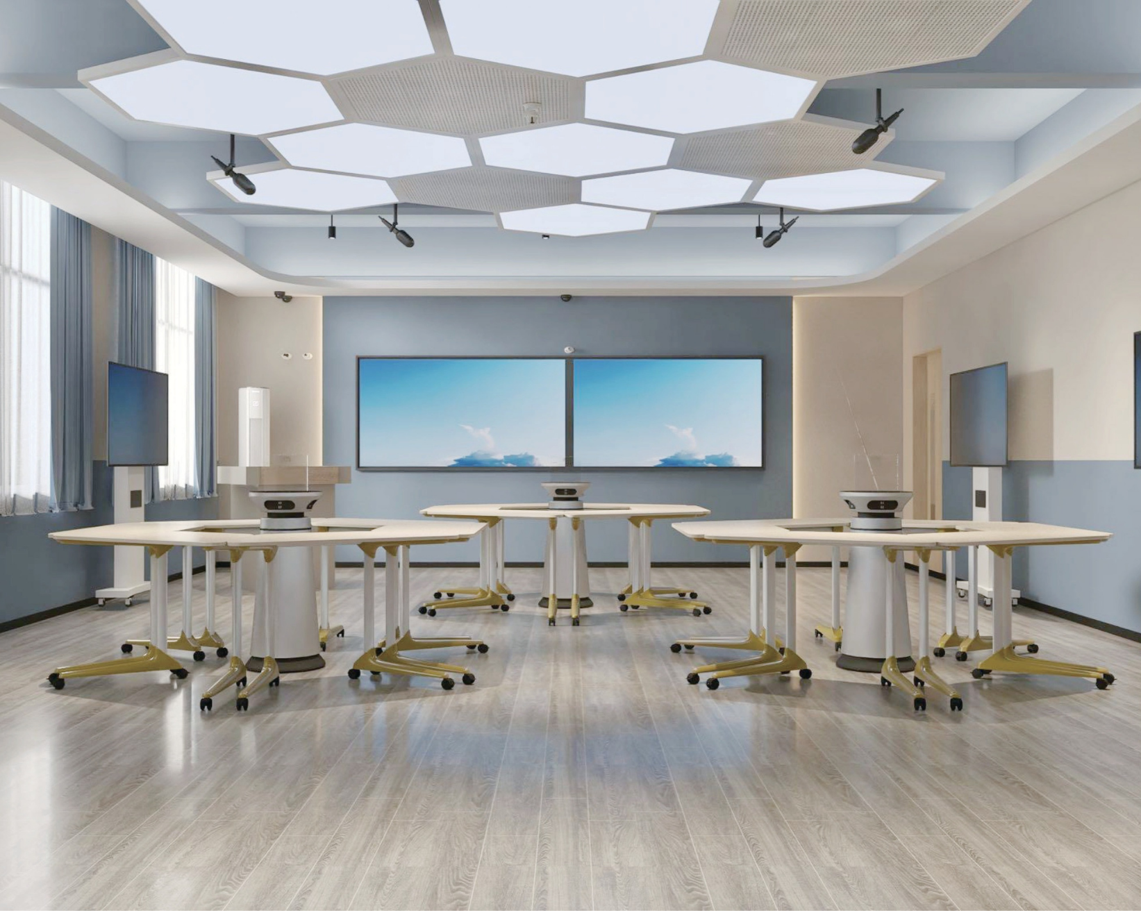 A modern conference room with a light wood floor, multiple tables with white surfaces and yellowish legs on wheels, and wall-mounted screens. The ceiling has large hexagonal light fixtures, and there are windows with light blue curtains on the left.
