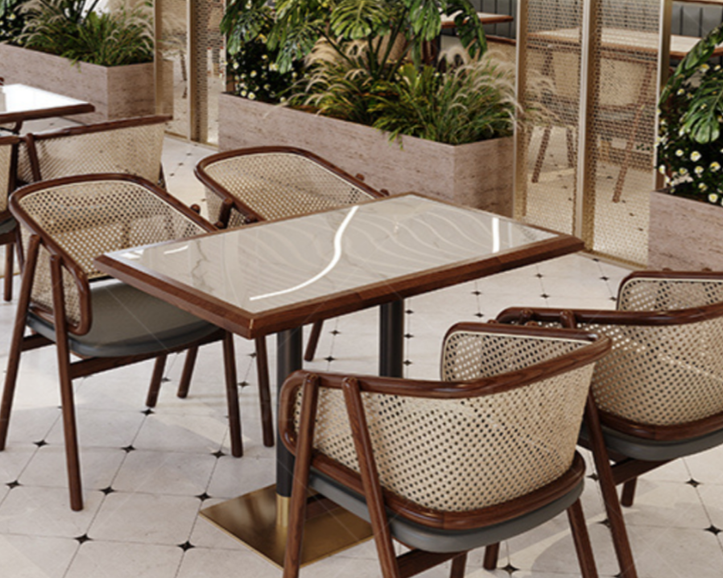 A restaurant patio with a square marble-topped table and six chairs with woven backs, surrounded by greenery and decorative fencing.