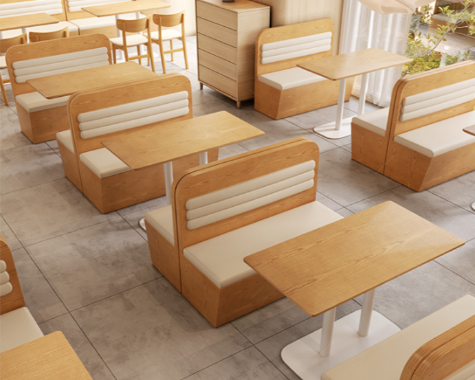 Indoor restaurant seating with wooden booths, white cushioned seats, and tables on a tiled floor with natural light.