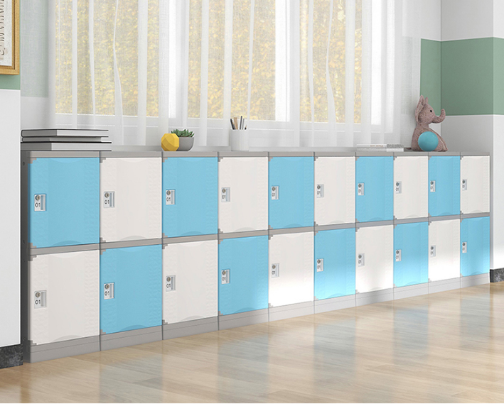 School lockers in blue and white with some toys and supplies on top, located along a wall by a window with yellow leaves outside.