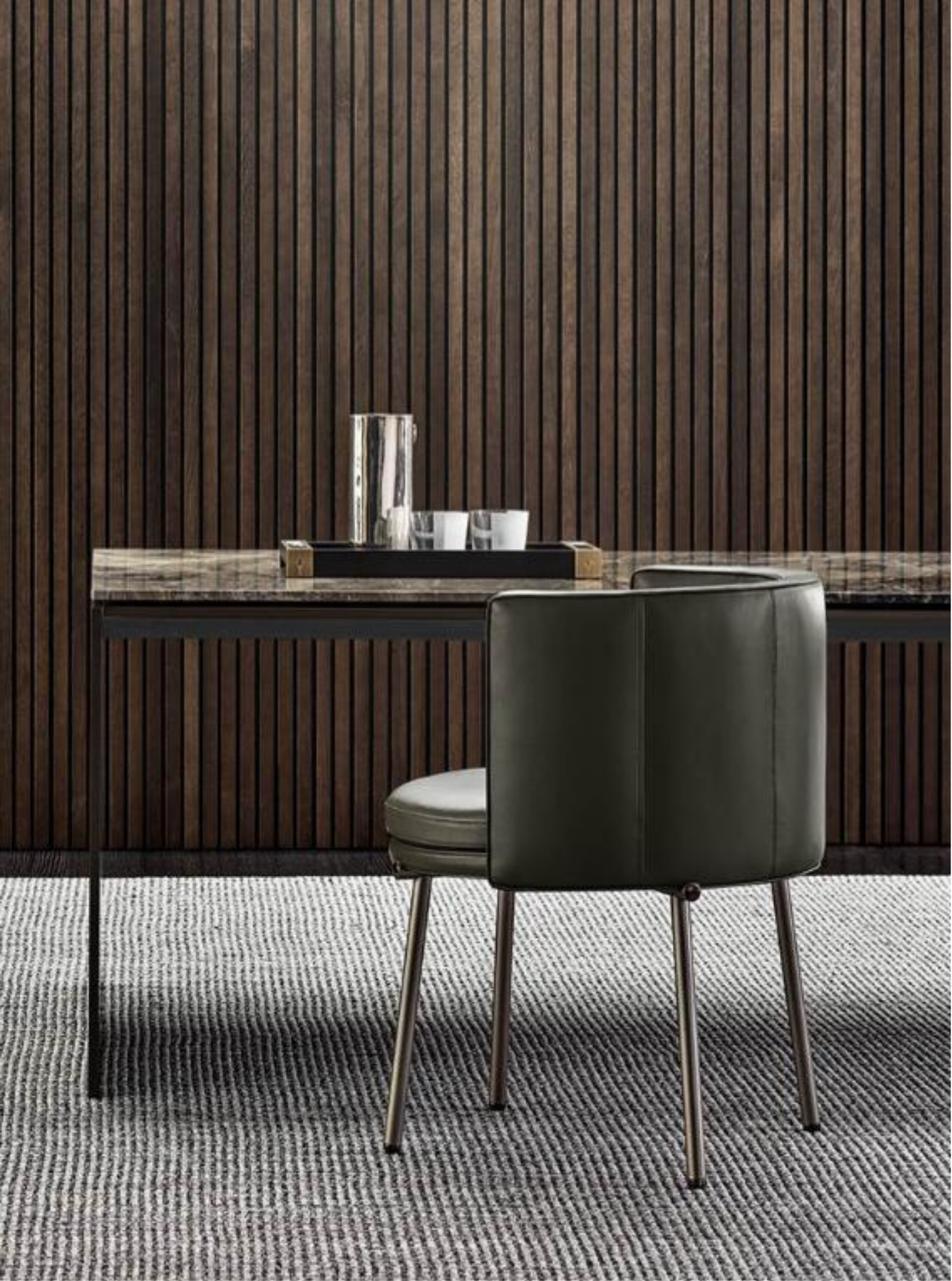 Modern office space with a dark wooden wall, a gray chair, a black tray with glassware, and a patterned carpet.