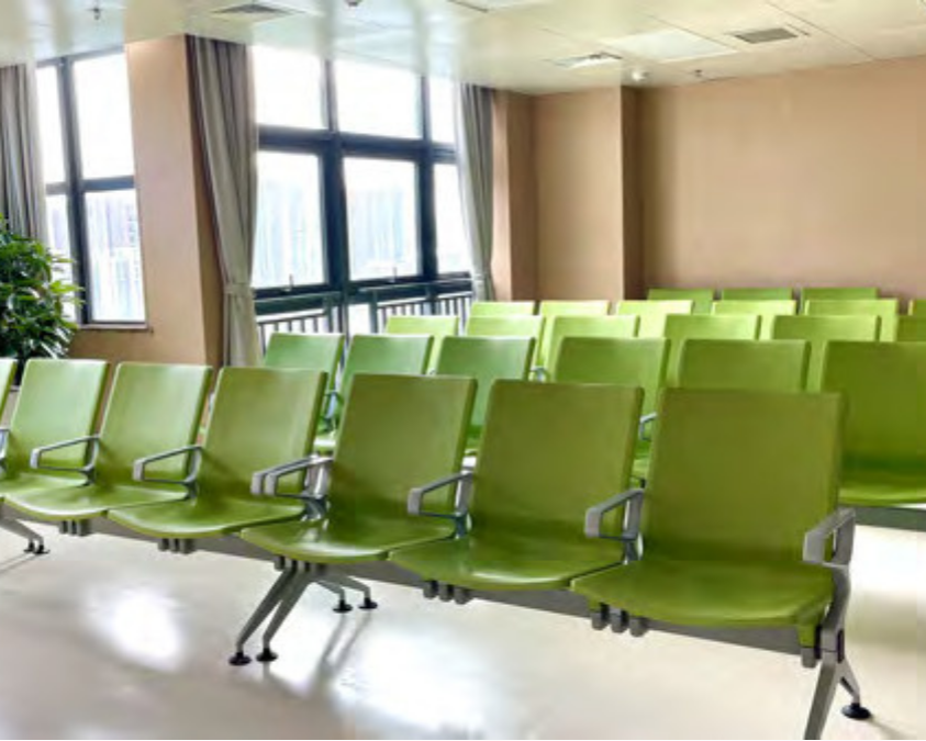 Empty green chairs in a waiting area with large windows and curtains.
