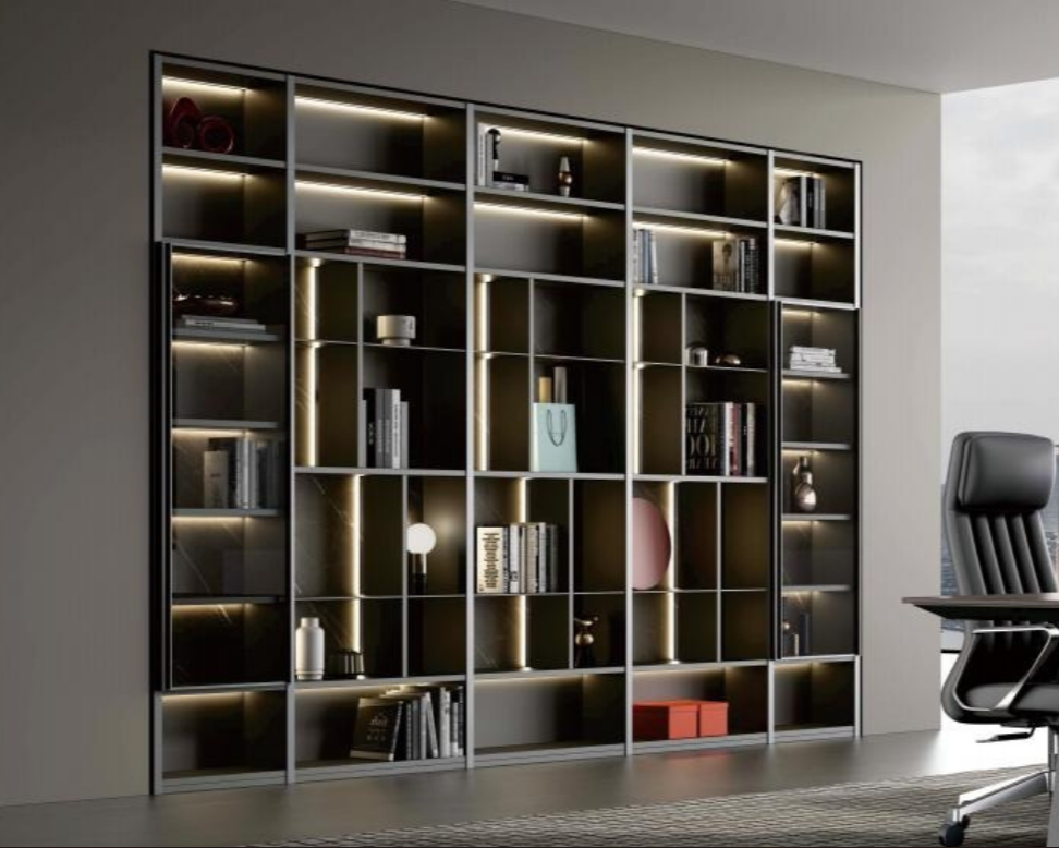 Modern black metal bookshelf with built-in LED lighting, filled with books, decorative items, and a pink and blue vase, situated next to a gray office chair in a contemporary workspace.