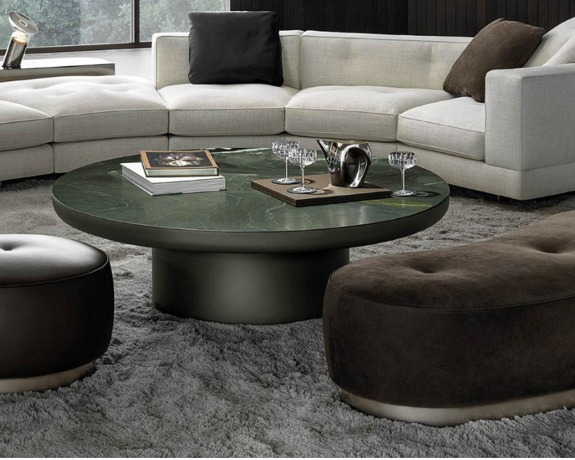 Modern living room with a round dark green coffee table, a white sectional sofa with black and brown pillows, and a plush gray rug.