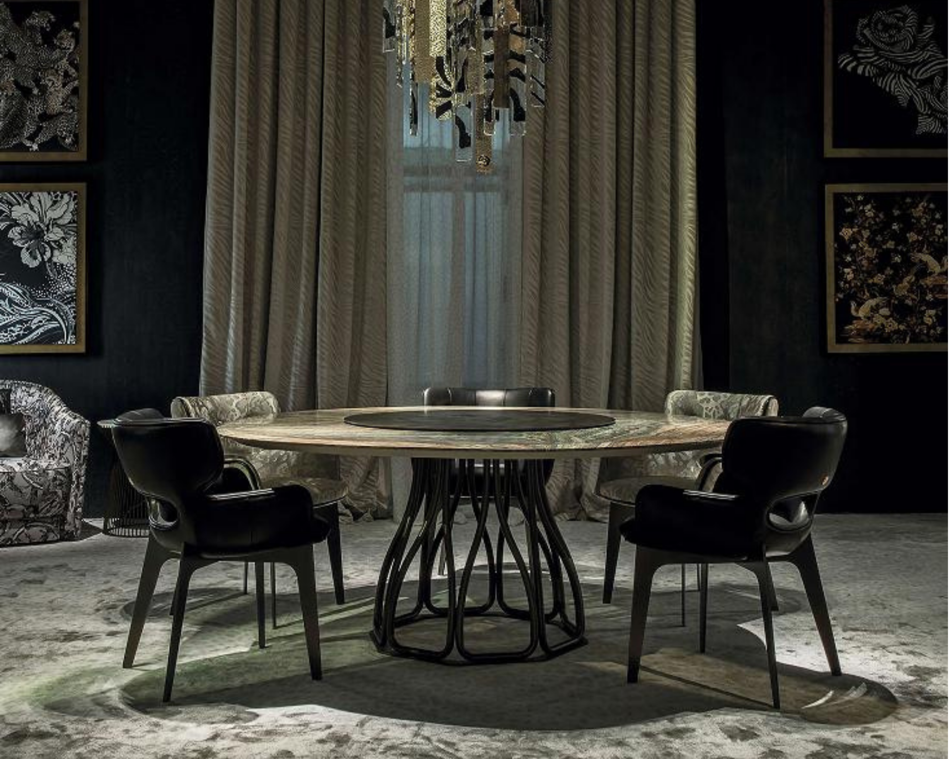 A dining room with a round table and eight dark chairs, a large chandelier, beige curtains, and framed black and gold artwork on dark walls.