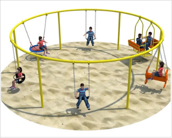 Children playing on a yellow circular swing set with sand underneath, some children sitting on swings, one child standing in the center, and others swinging.
