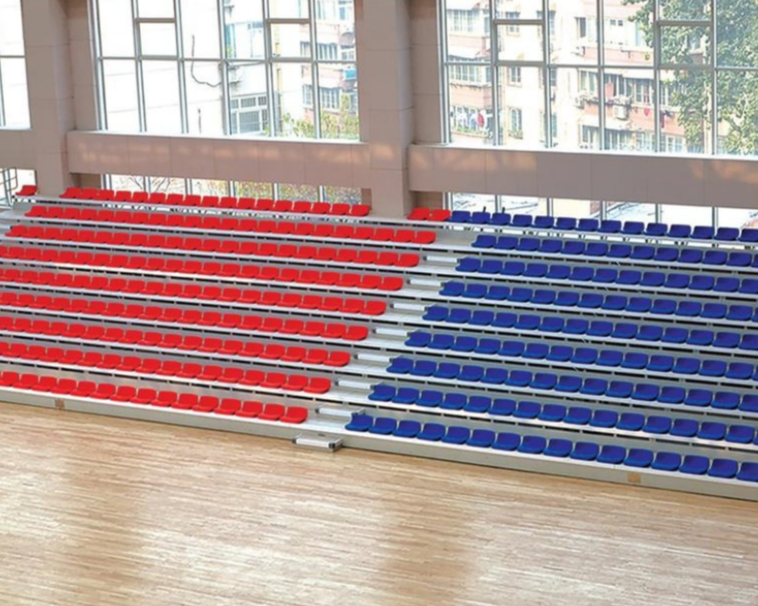Colorful stadium seats with red and blue chairs inside a gymnasium with large windows and a wooden floor.